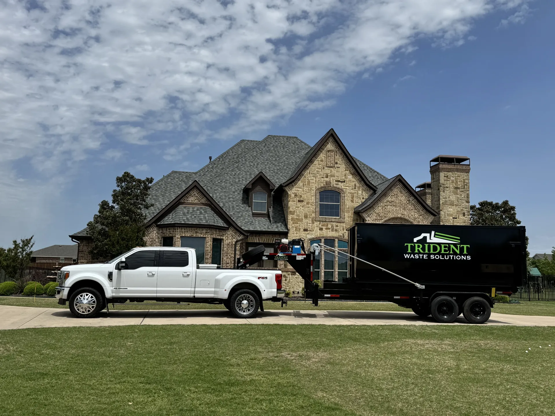 A green dumpster is parked in front of a house.