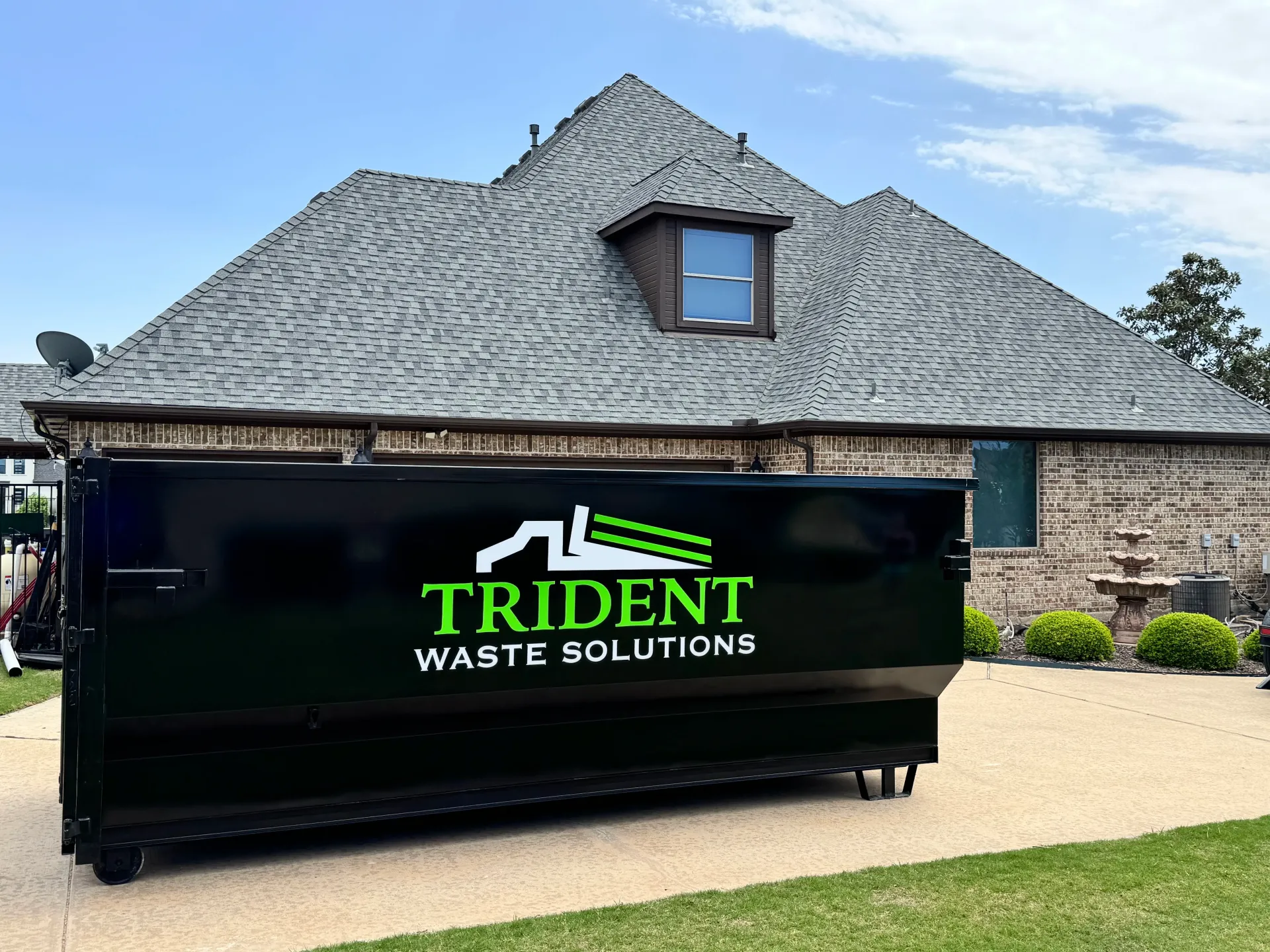 A dumpster is being towed by a dump truck in a driveway.