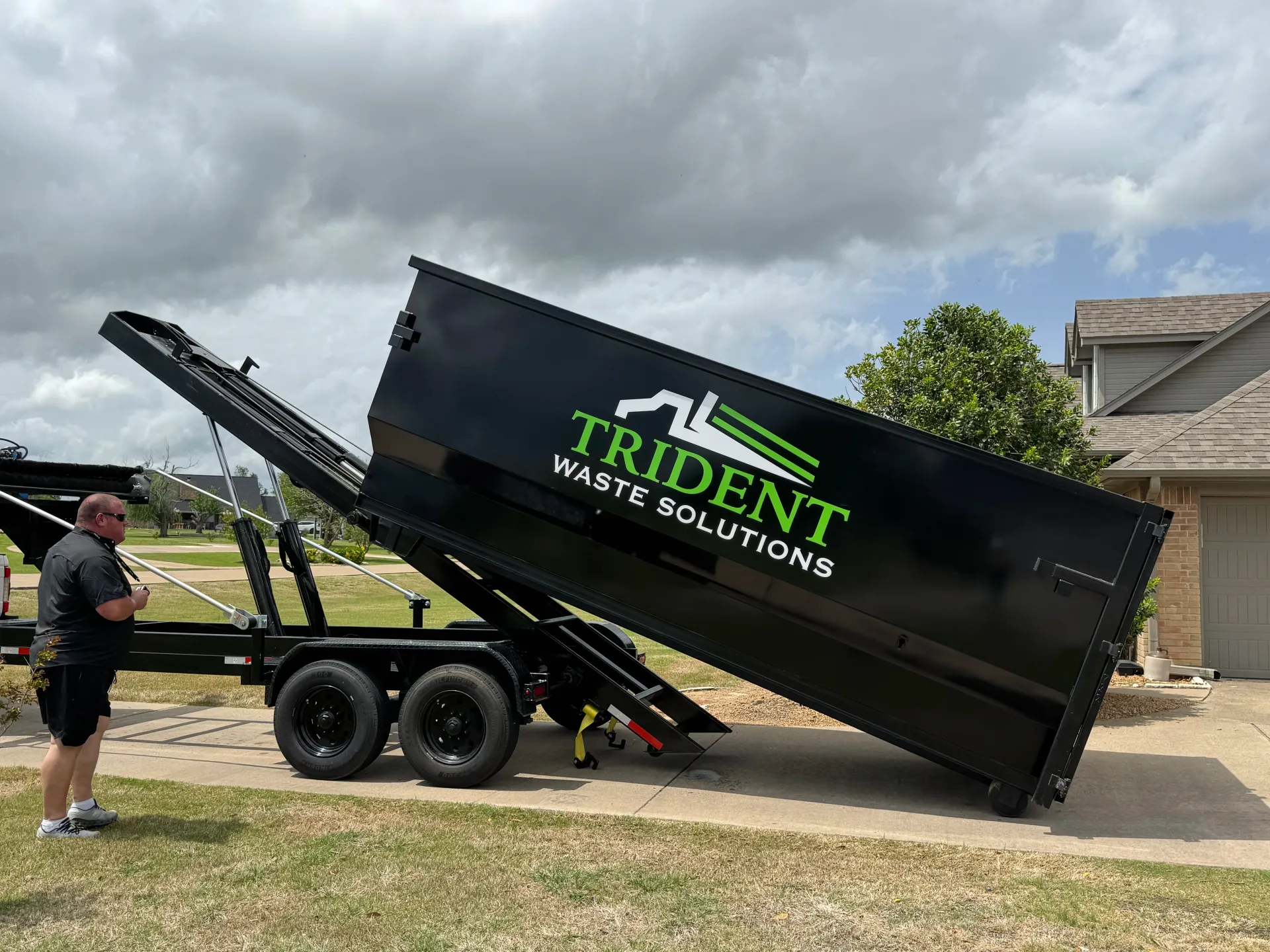 A green dumpster is sitting in front of a garage.