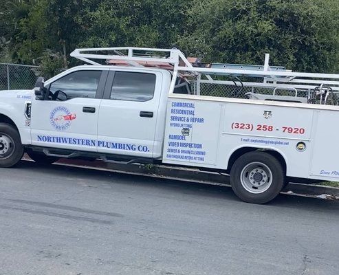 White plumbing truck parked on the street with the Northwestern Plumbing Co. logo. Phone number is visible.