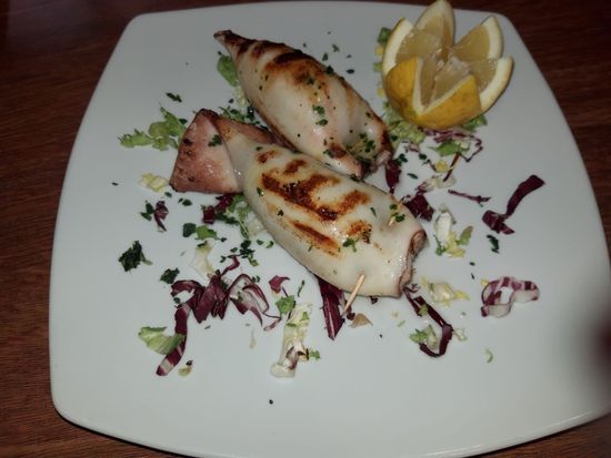 Un piatto bianco condito con calamari grigliati e fette di limone