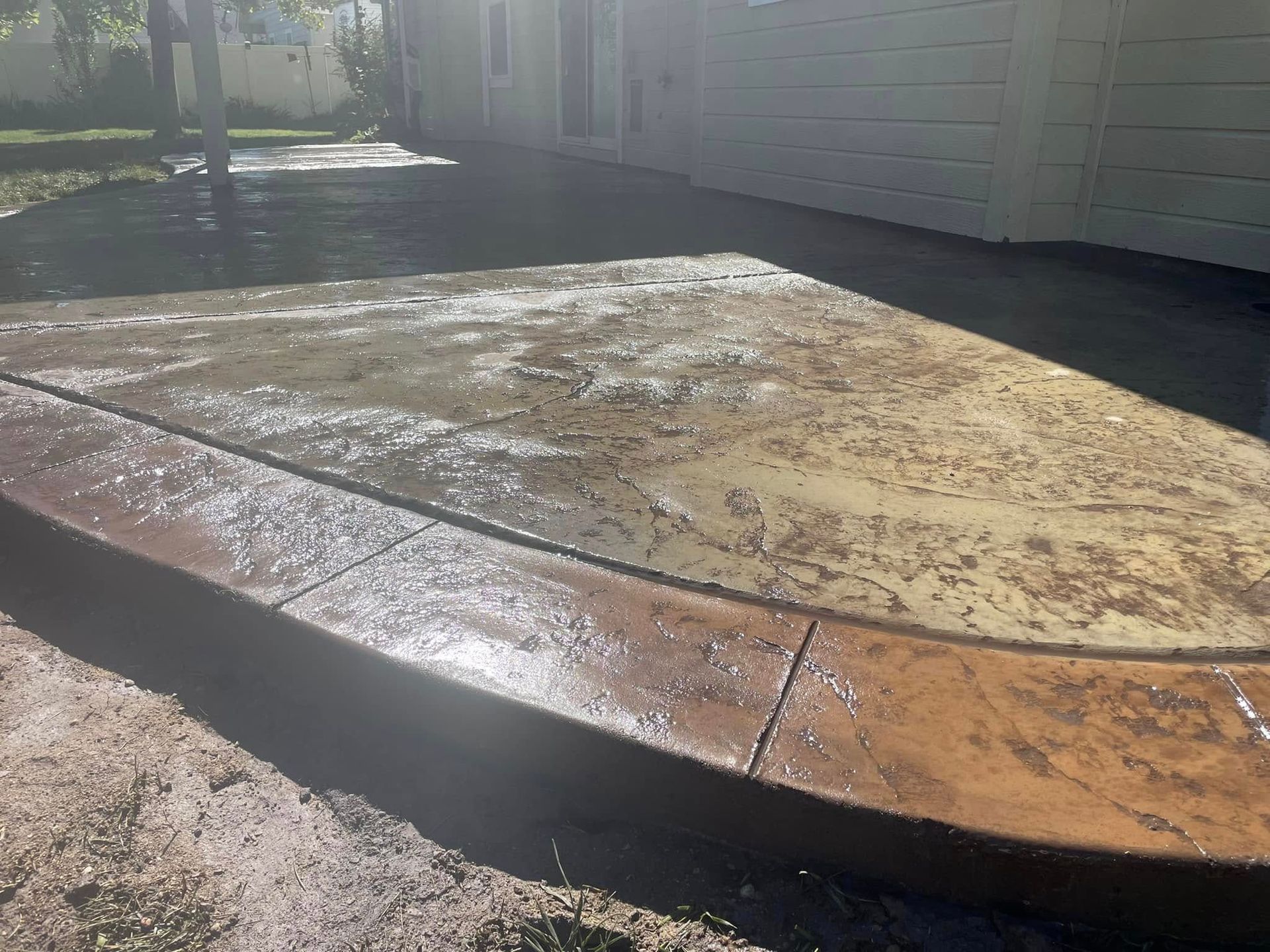 Freshly stained concrete patio with wet surface and sunny yard beside a house