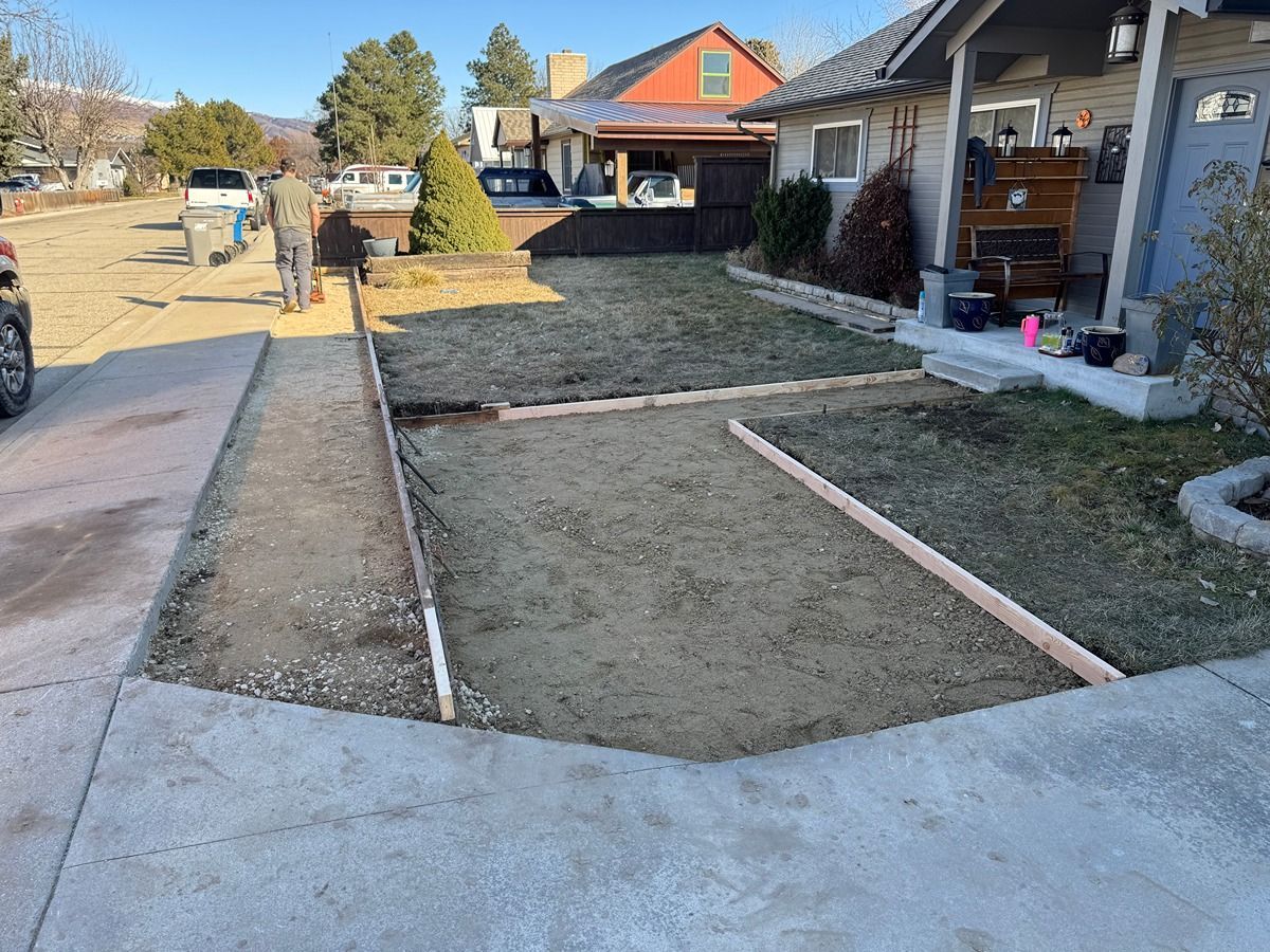 Front yard under construction with fresh concrete walkway and leveled dirt beside a house