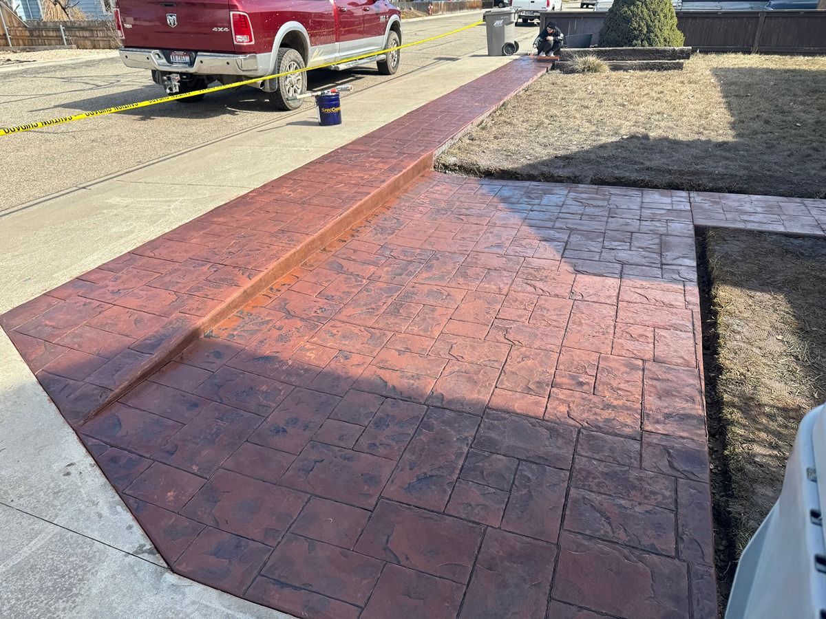 Red brick walkway under construction beside a driveway, with caution tape and a red truck nearby.
