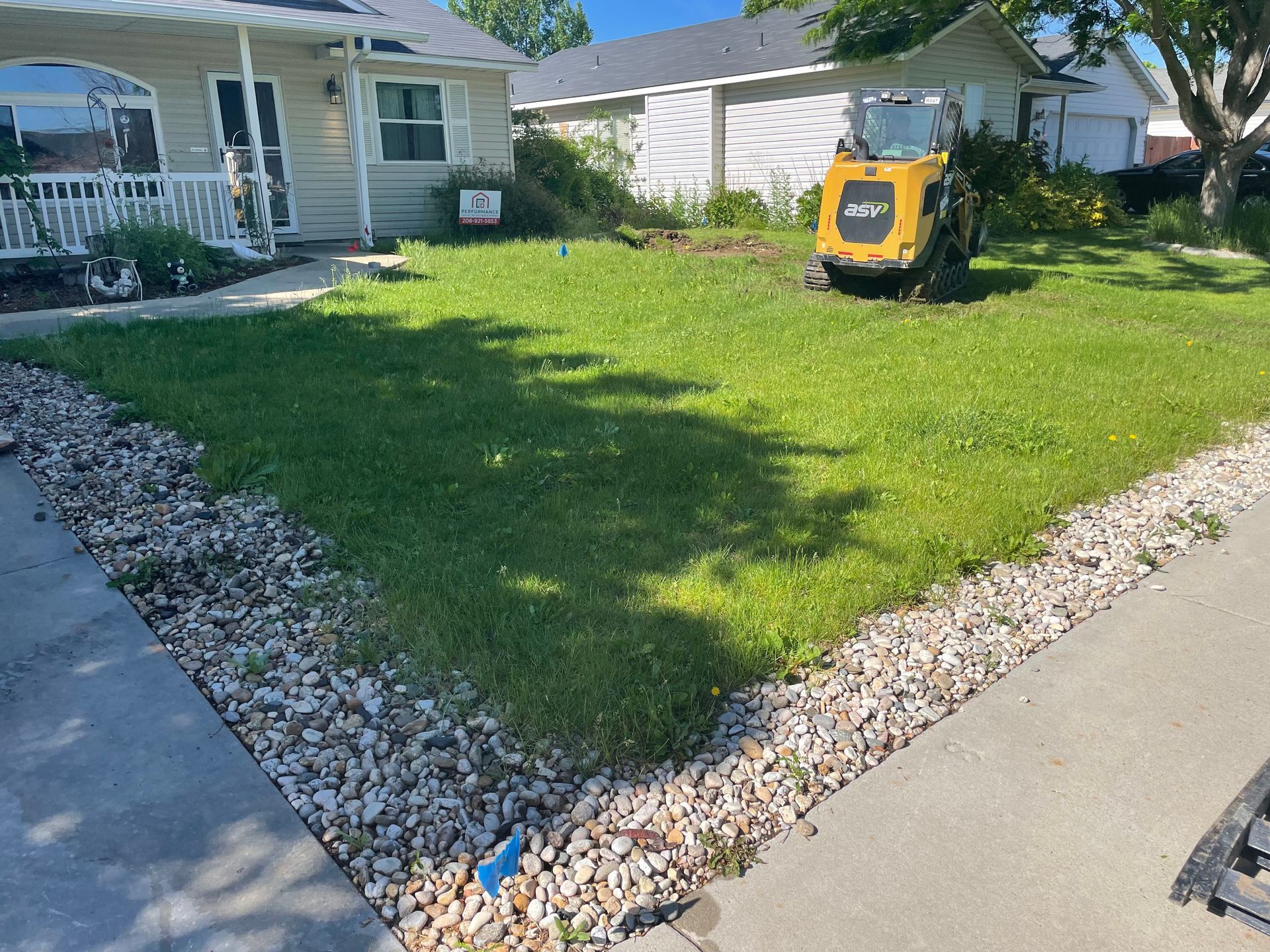 Small front yard with green grass, a yellow lawn machine, and a house in the background.