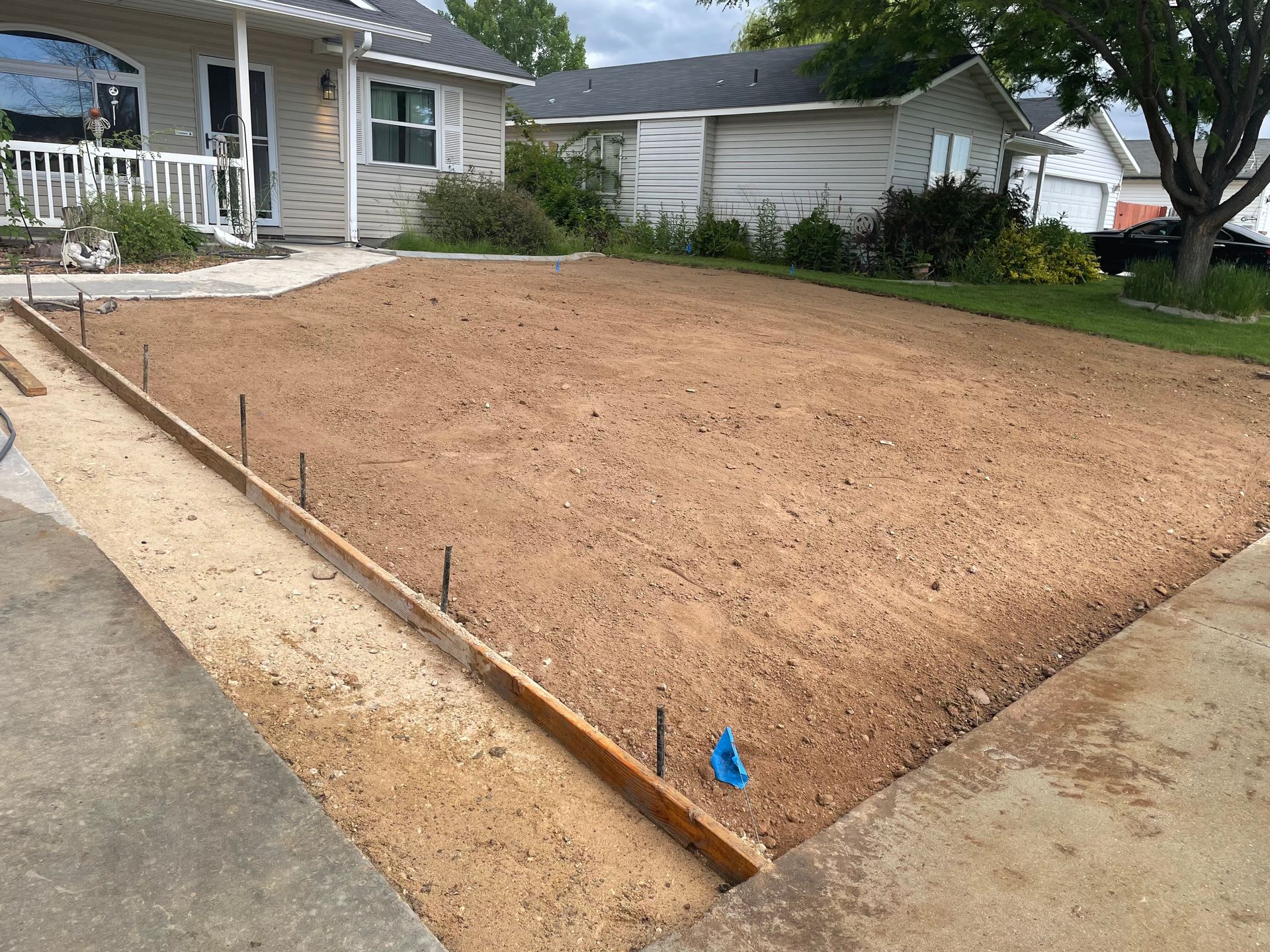 Newly graded dirt yard beside a house, bordered by wooden edging and concrete driveway.