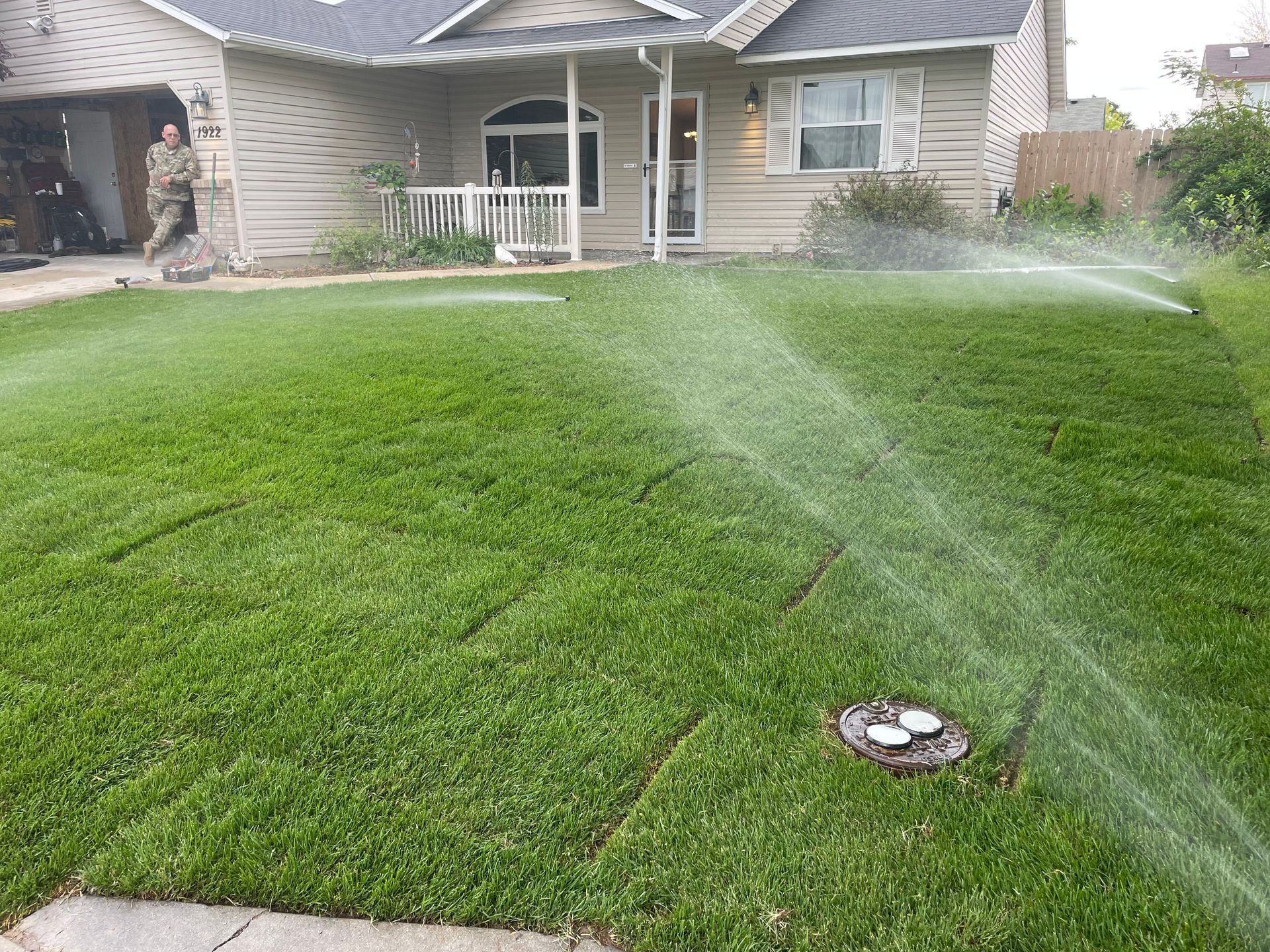 Lawn sprinkler watering a green backyard in front of a house