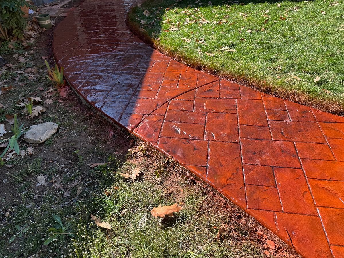 Red and black tiled curved garden path beside grass and fallen leaves