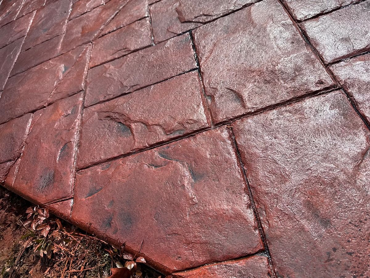 Cracked red concrete pavement with moss along the edge