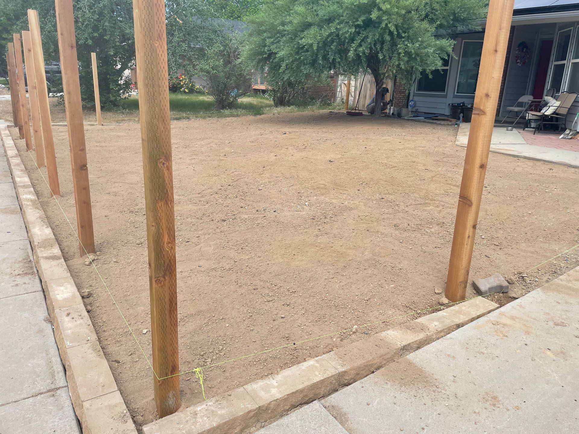 New gravel yard bordered by wooden posts and a concrete edge, with trees and a house in the background