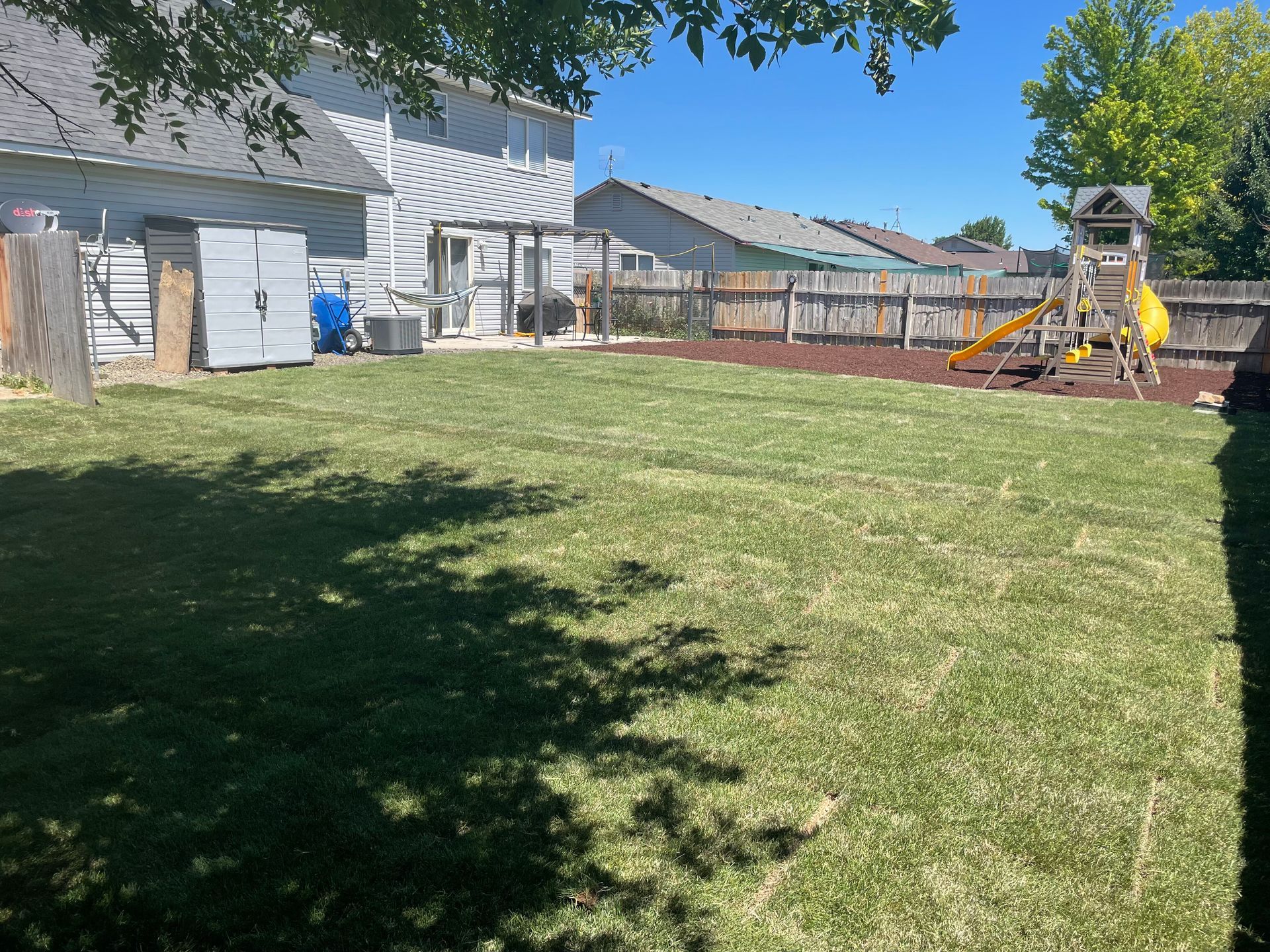 Backyard with green lawn, white house, and children’s playset under a clear blue sky