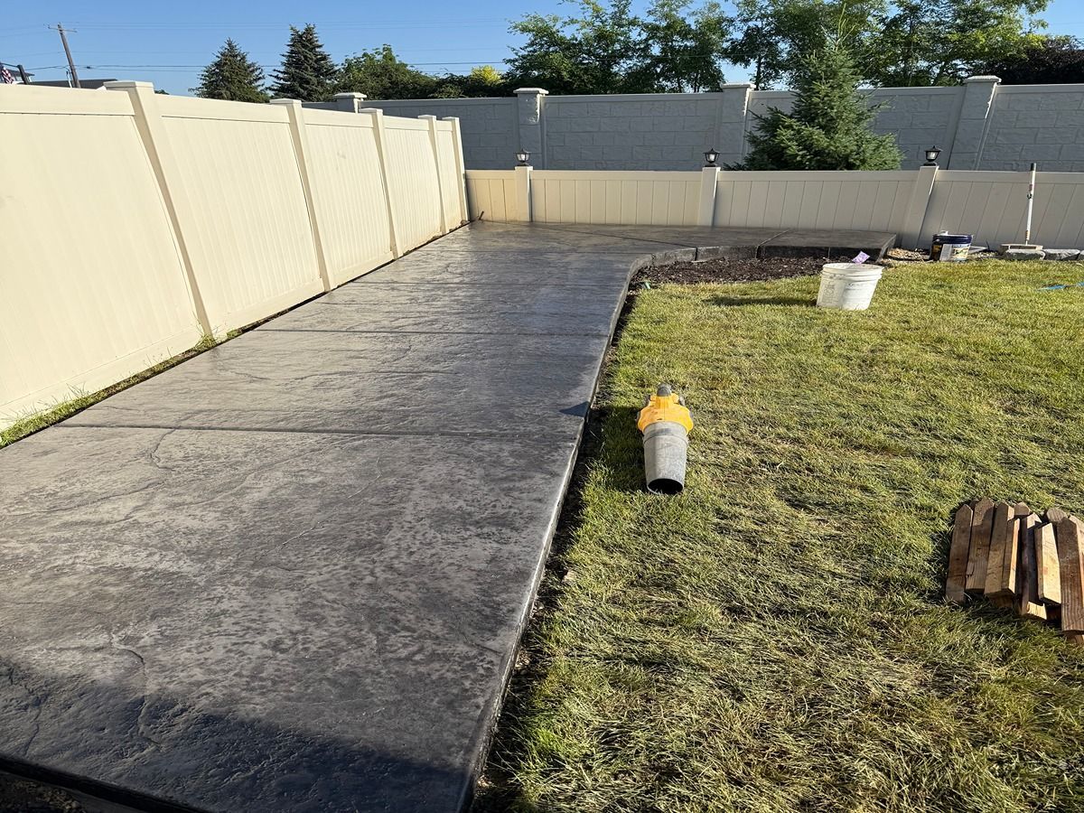 Backyard with a concrete path, grassy yard, and stacked fence panels under a clear sky