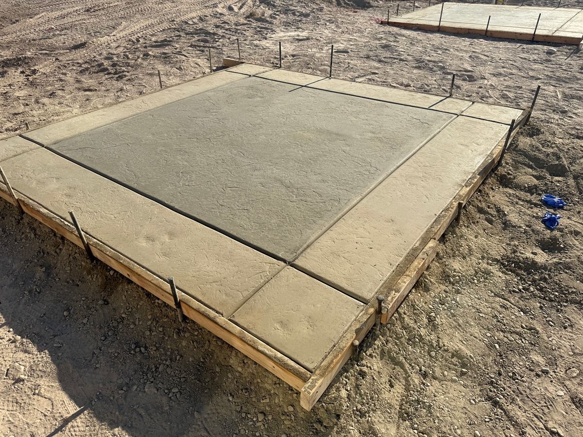 Fresh concrete slab in a dirt lot, framed by light wood forms.