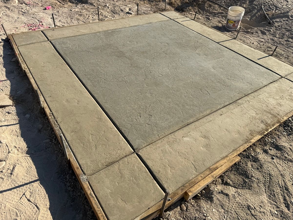 Freshly poured concrete slab with smooth gray center and rough tan border on a dirt construction site