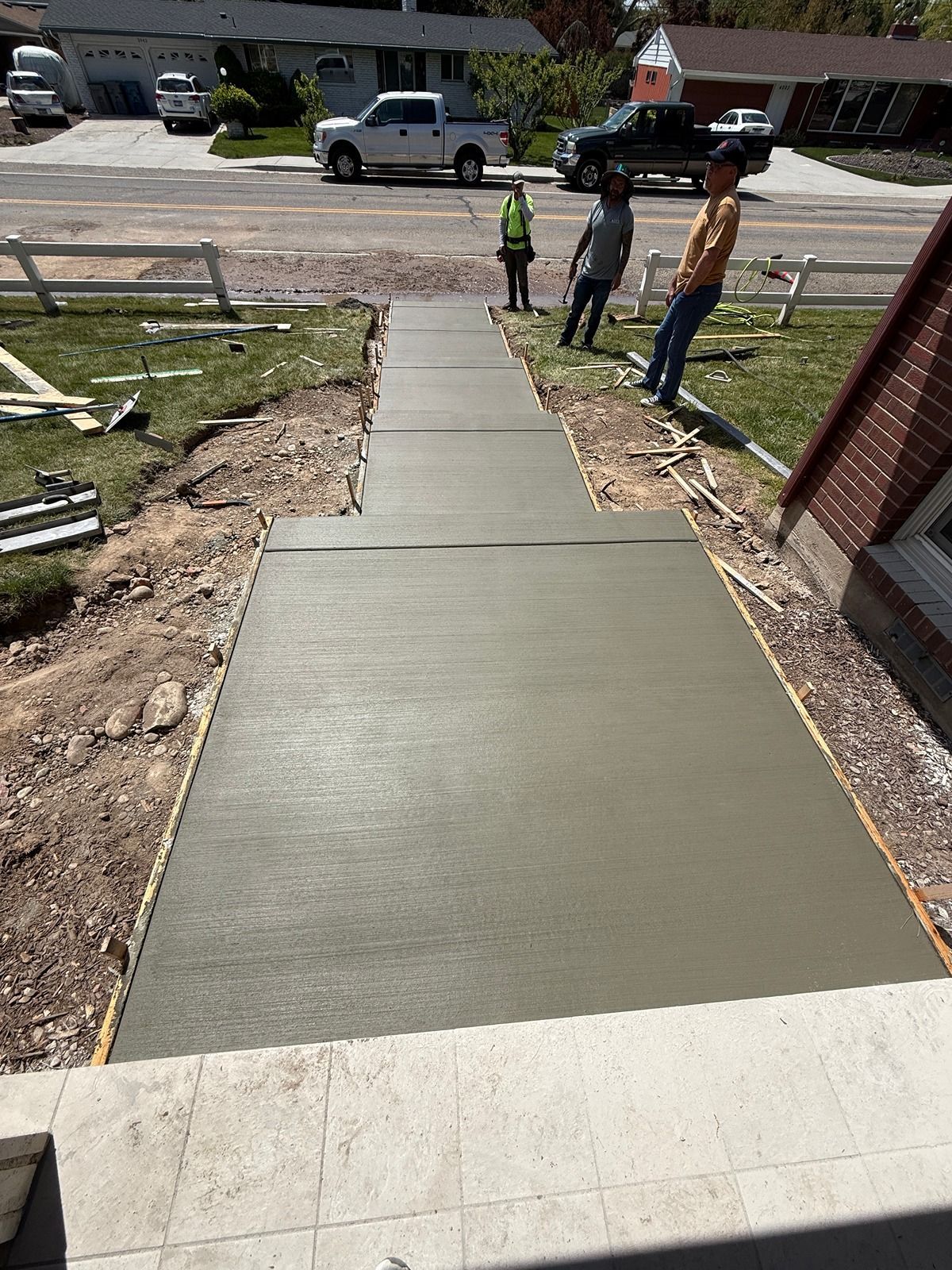 Fresh concrete walkway leading to a street, with workers and a white van in the background.