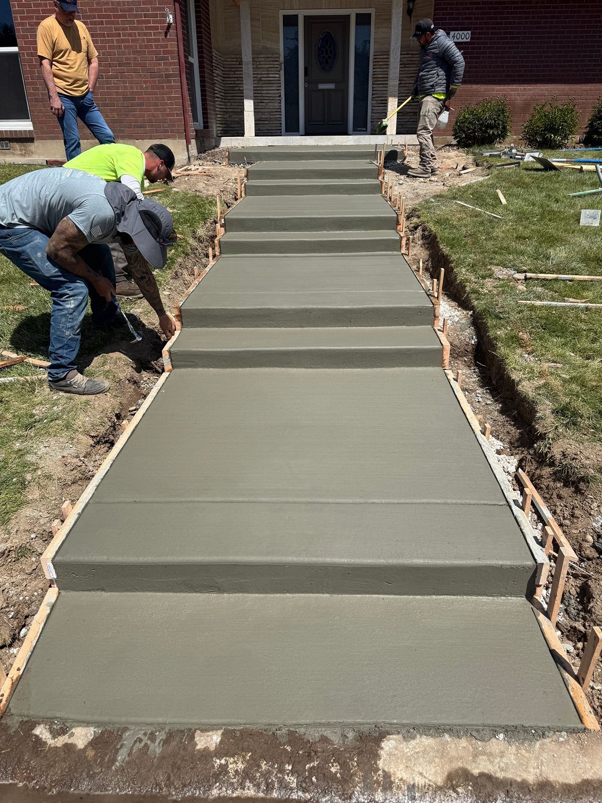 Workers pouring fresh concrete for a front walkway leading to a house entrance.