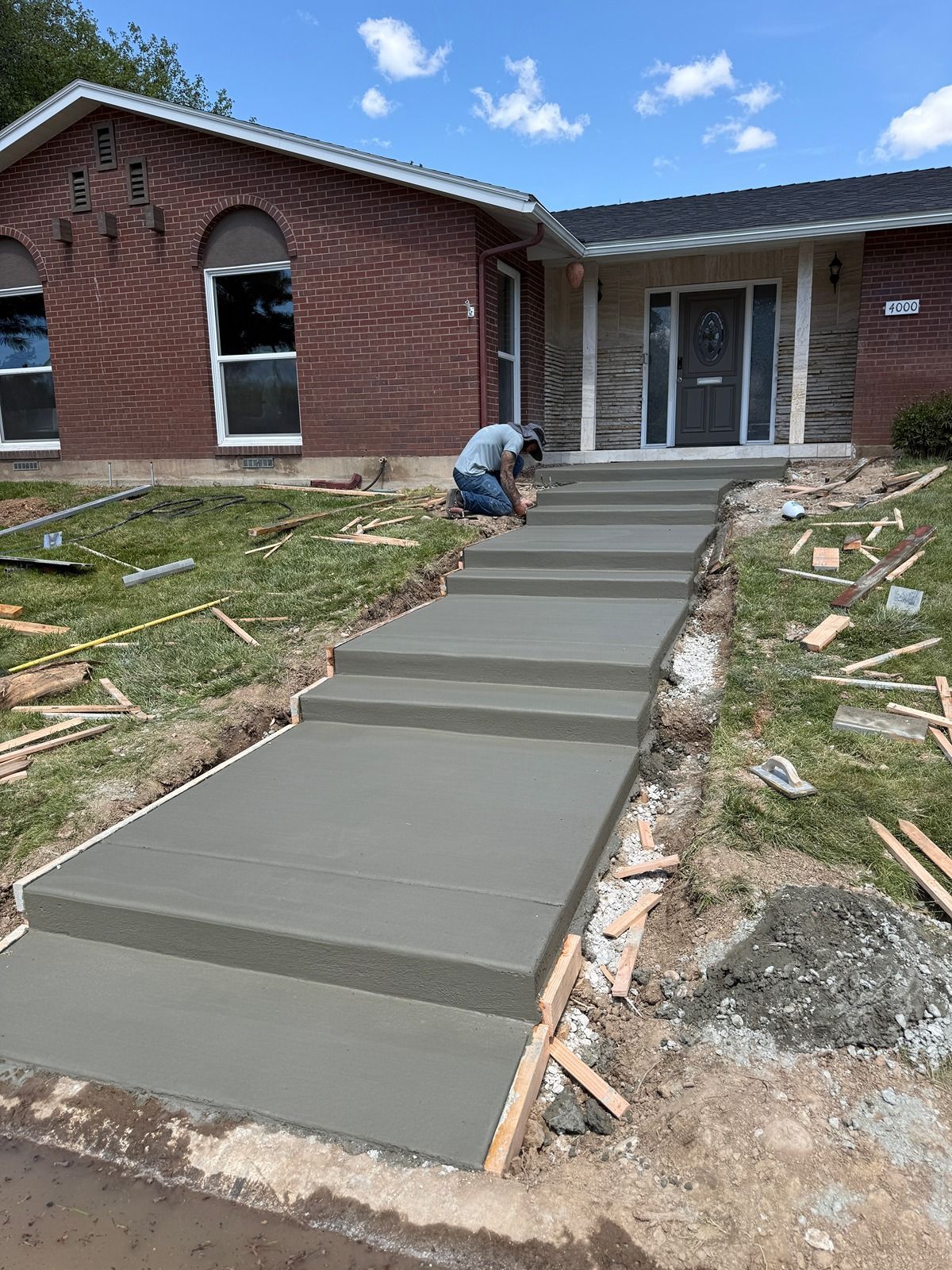 Worker pouring concrete for a front walkway at a brick house
