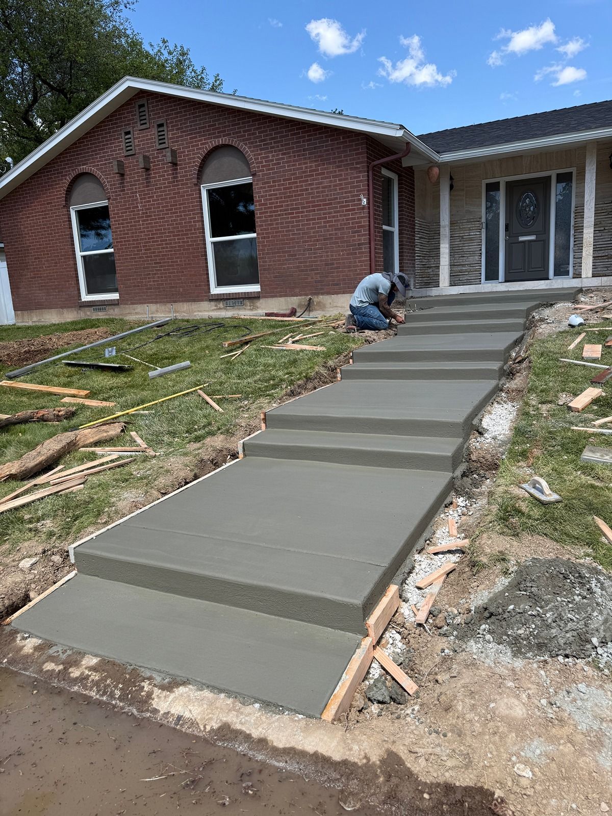 Concrete walkway under construction leading to a brick house, with a worker smoothing fresh concrete.