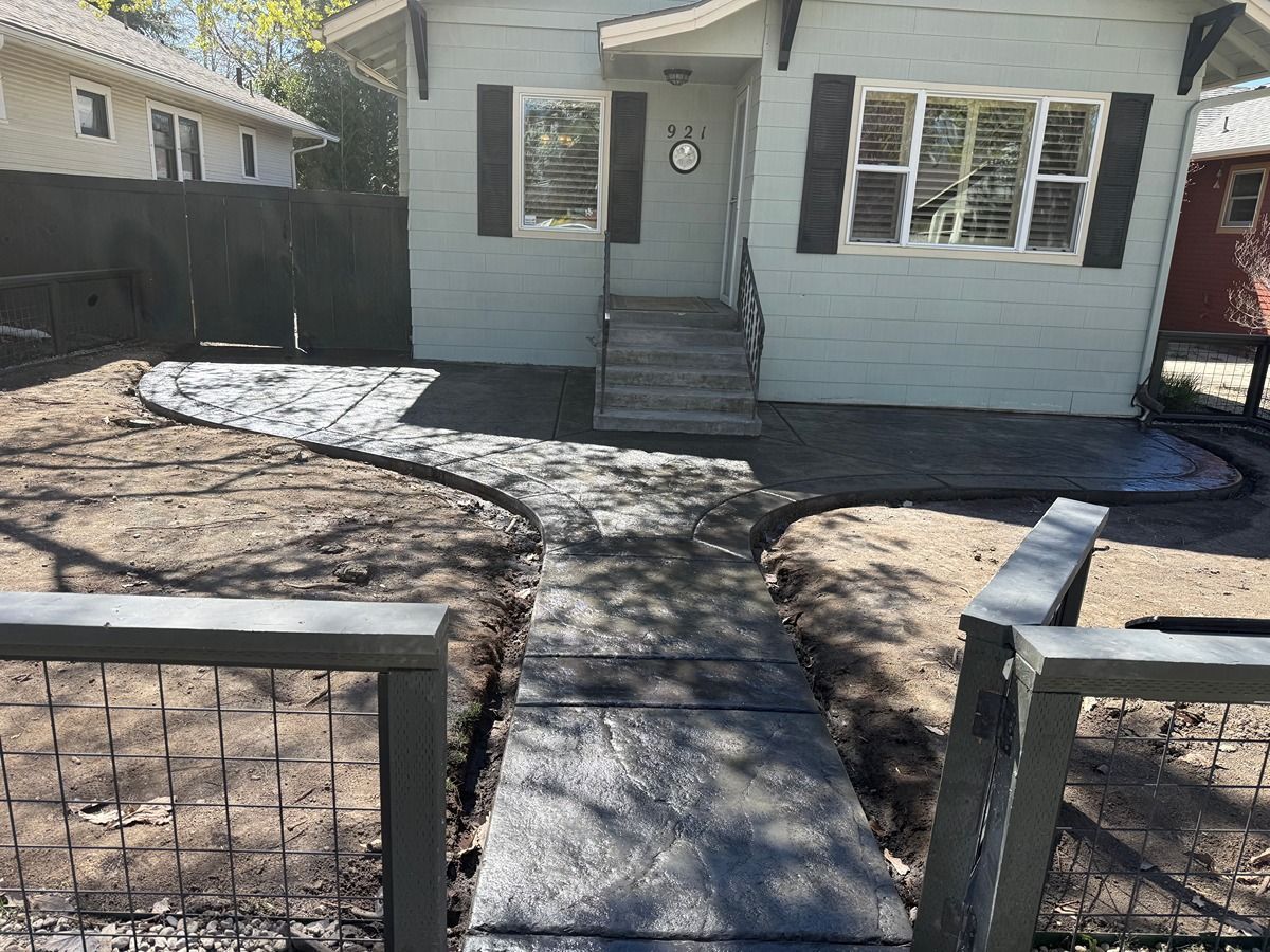Front yard with a concrete walkway leading to a light blue house and small front steps, framed by a gate.