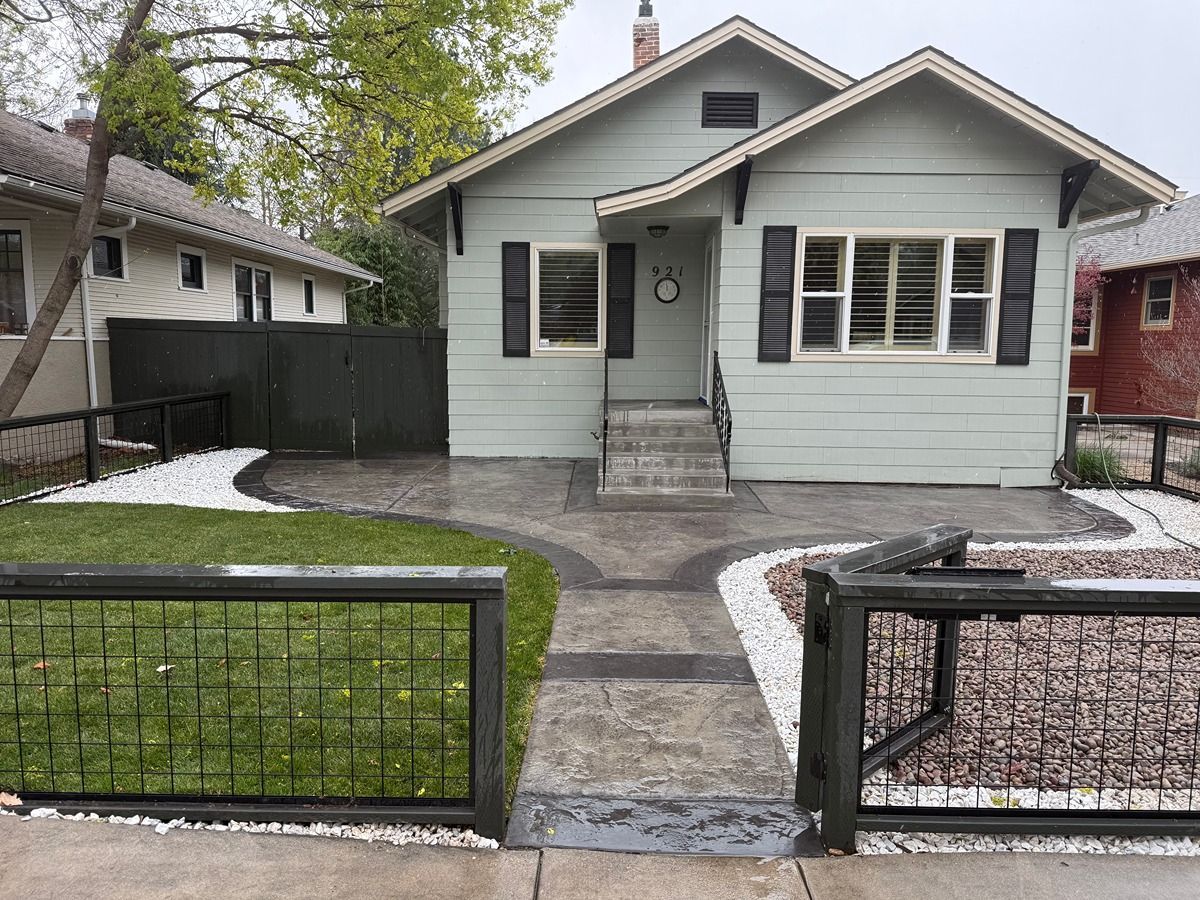 Small gray house with a front porch, walkway, fenced yard, and patches of snow.