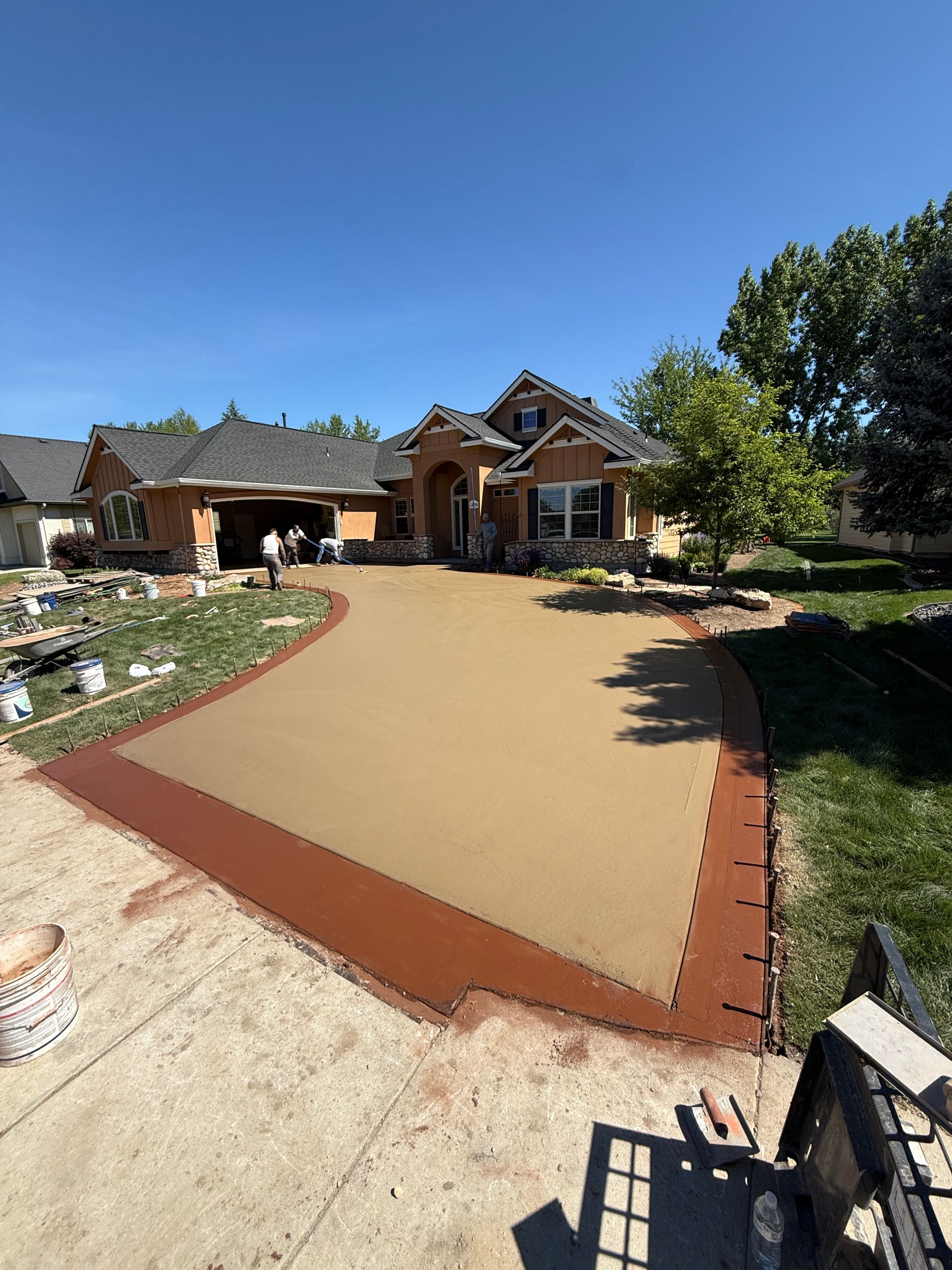 New concrete driveway leading to a brick house with a clear blue sky and landscaped yard