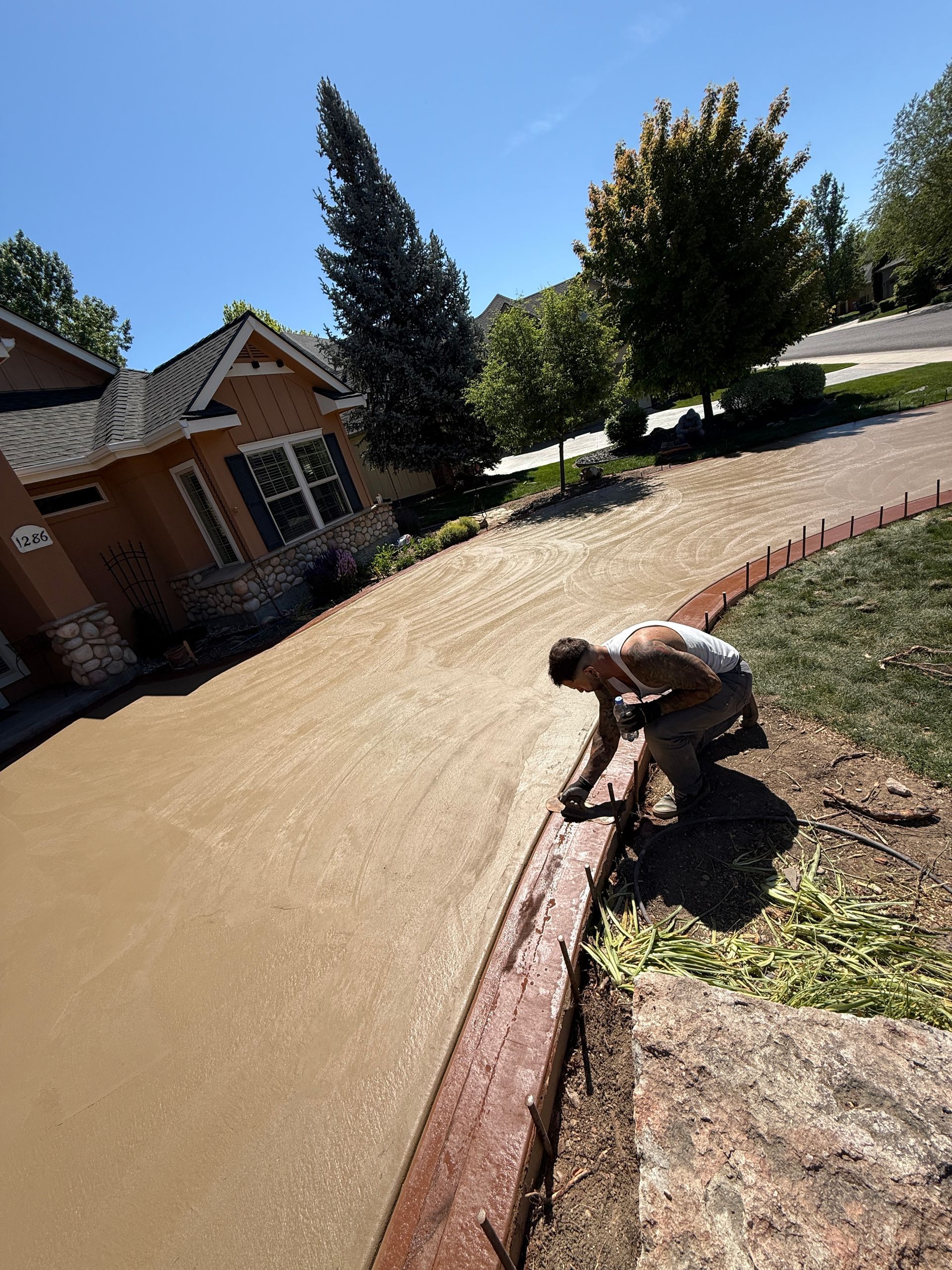 Person digging along a curved brick driveway in front of a house on a sunny day