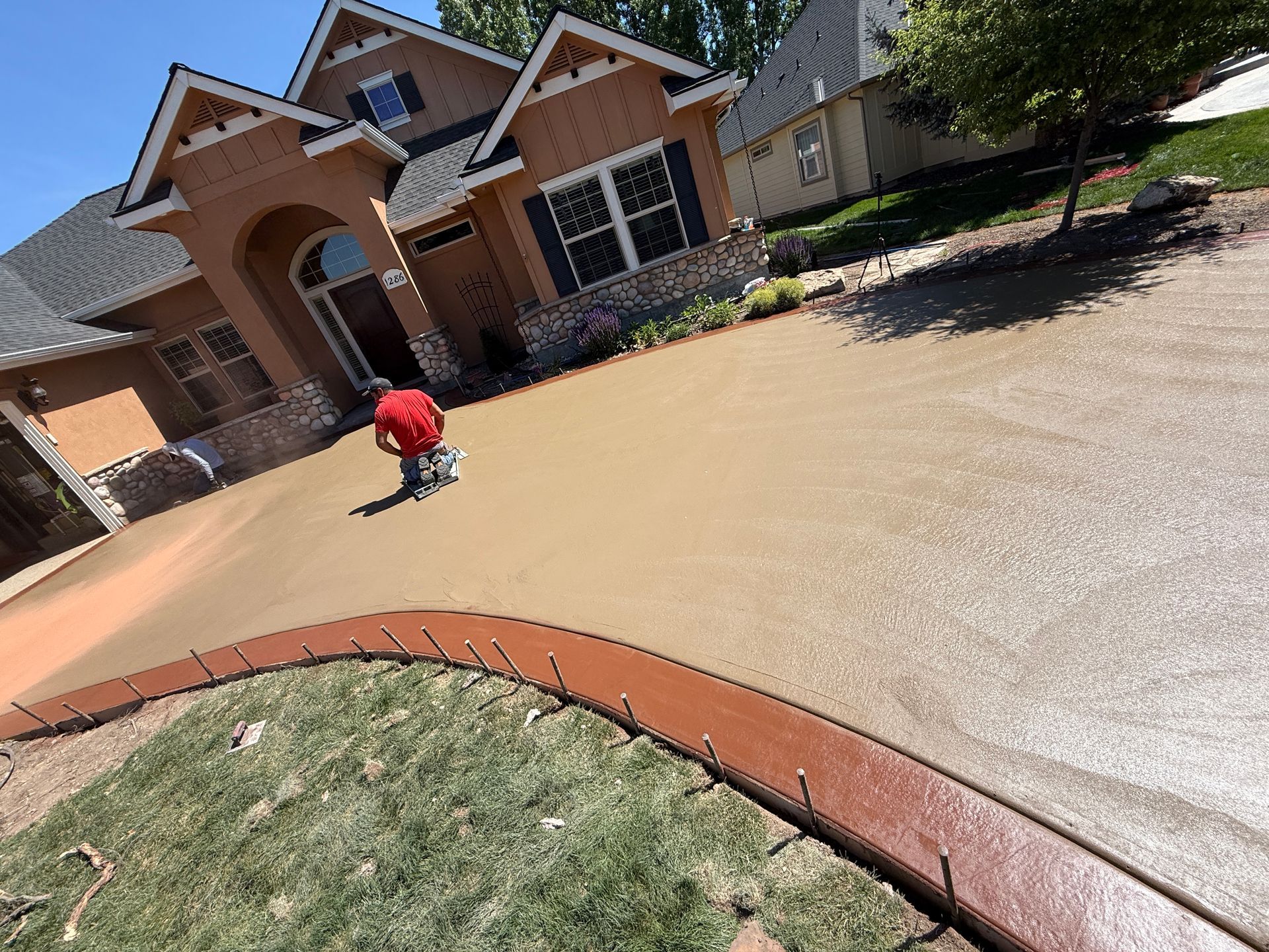 Child in a red shirt crouching on a driveway in front of a suburban house