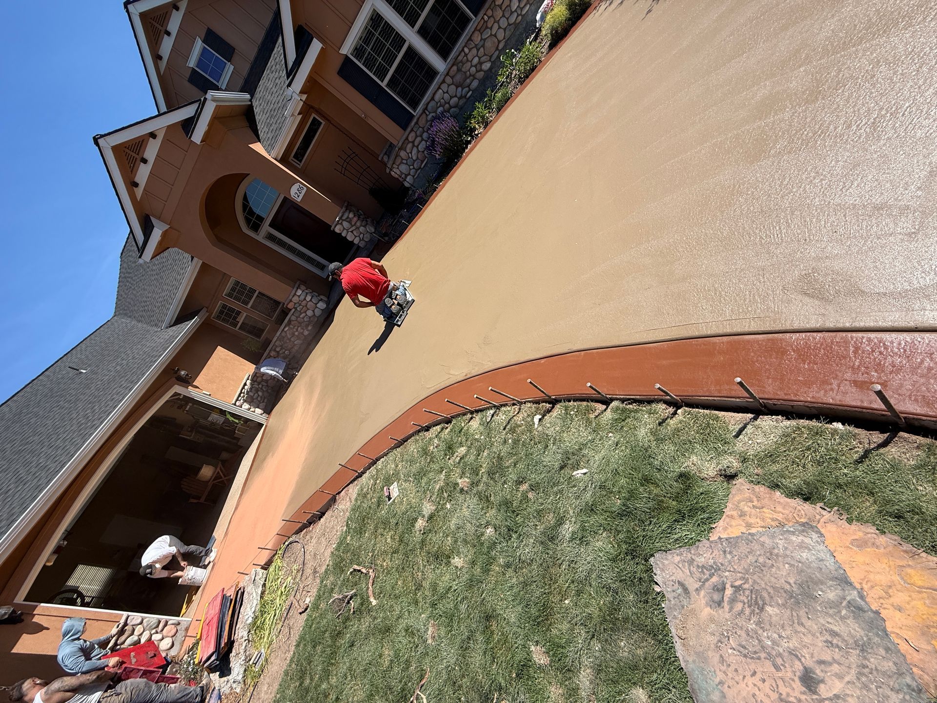 Tilted view of a brick house and driveway with a person in a red shirt walking across the courtyard.