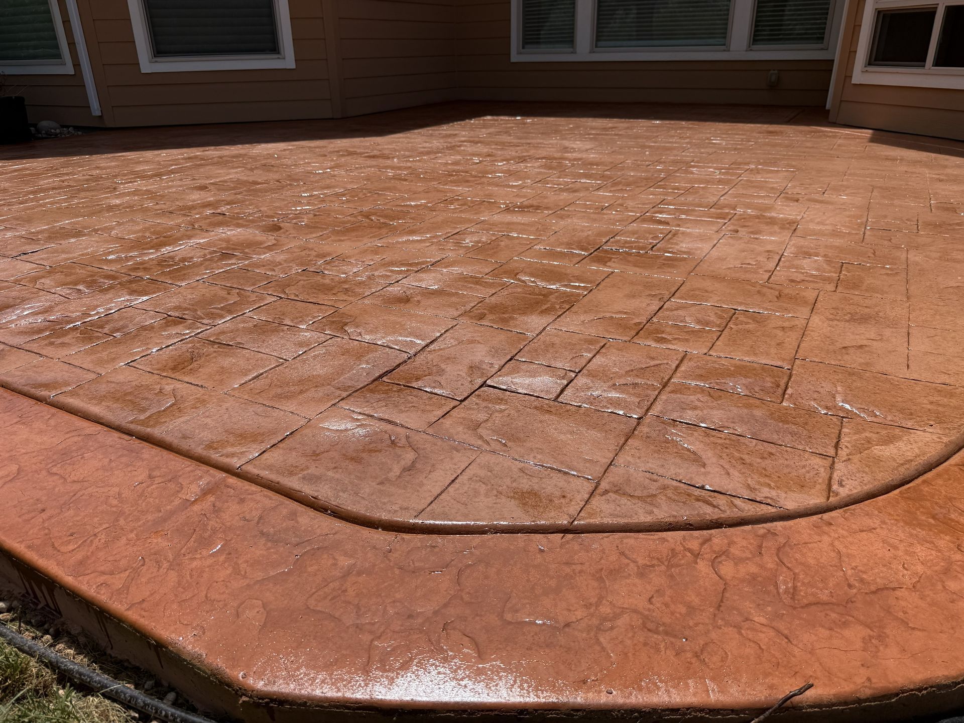 Stamped concrete patio with a curved step edge, wet from water spray in front of a house