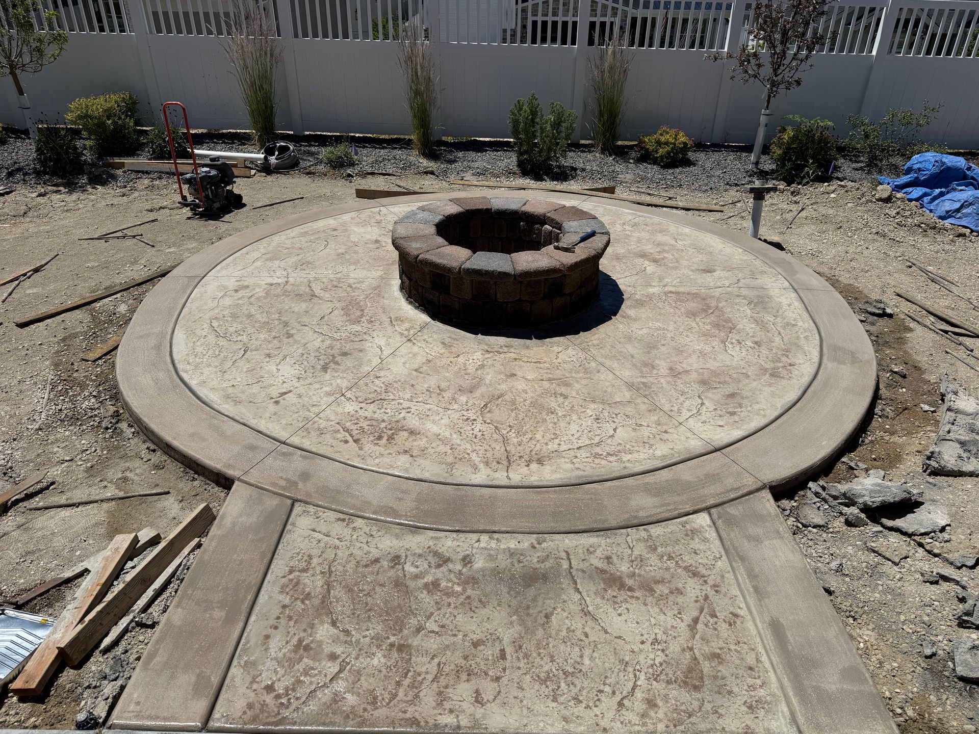 Concrete fire pit centered in a circular patio under construction, surrounded by dirt and fencing.