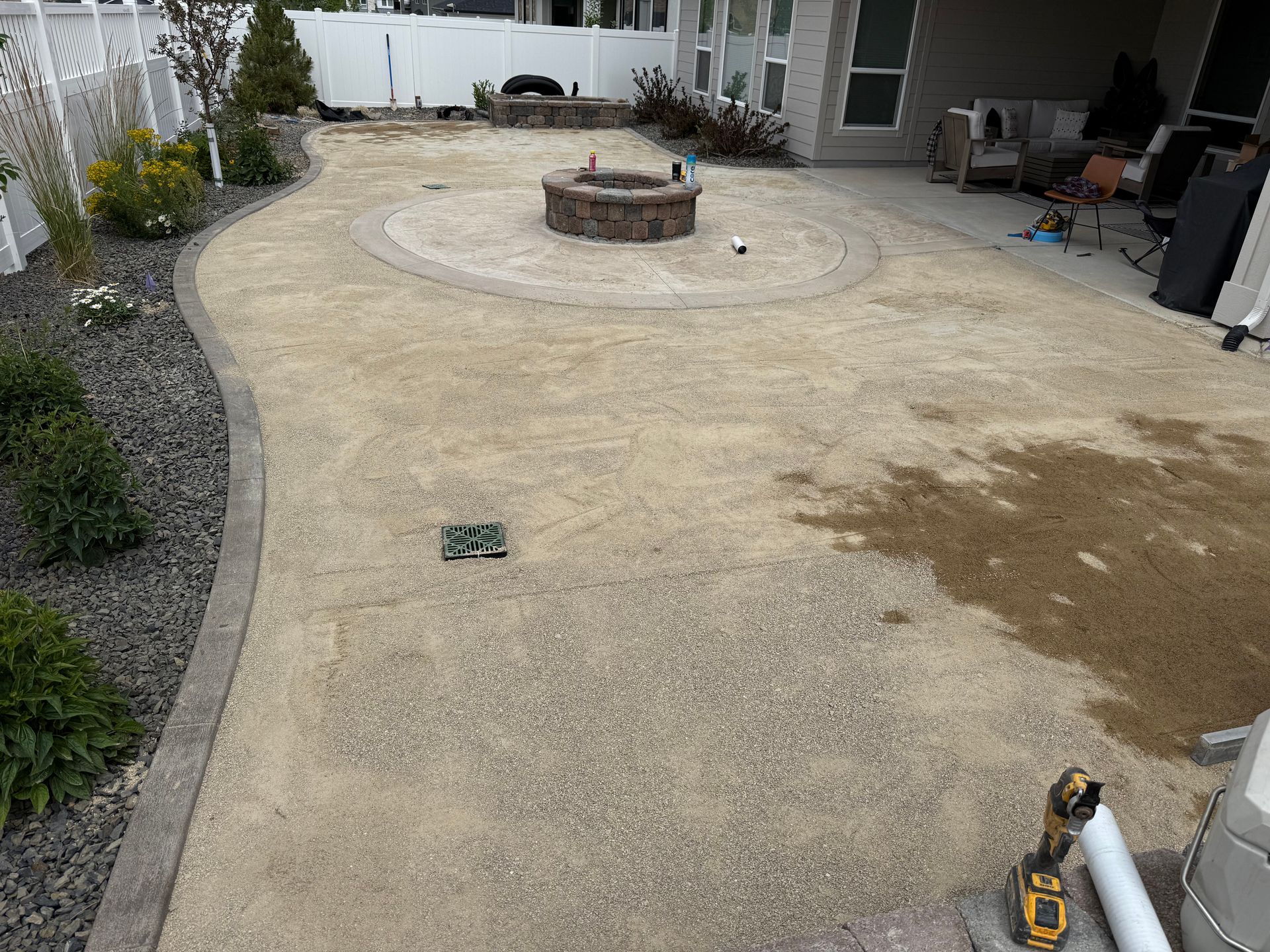 Backyard patio with a circular stone fire pit and gravel borders, viewed from a house patio doorway