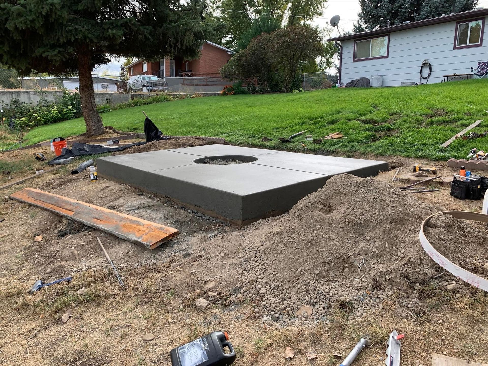 Concrete septic tank or utility vault set in a dirt yard, with tools and lumber nearby.