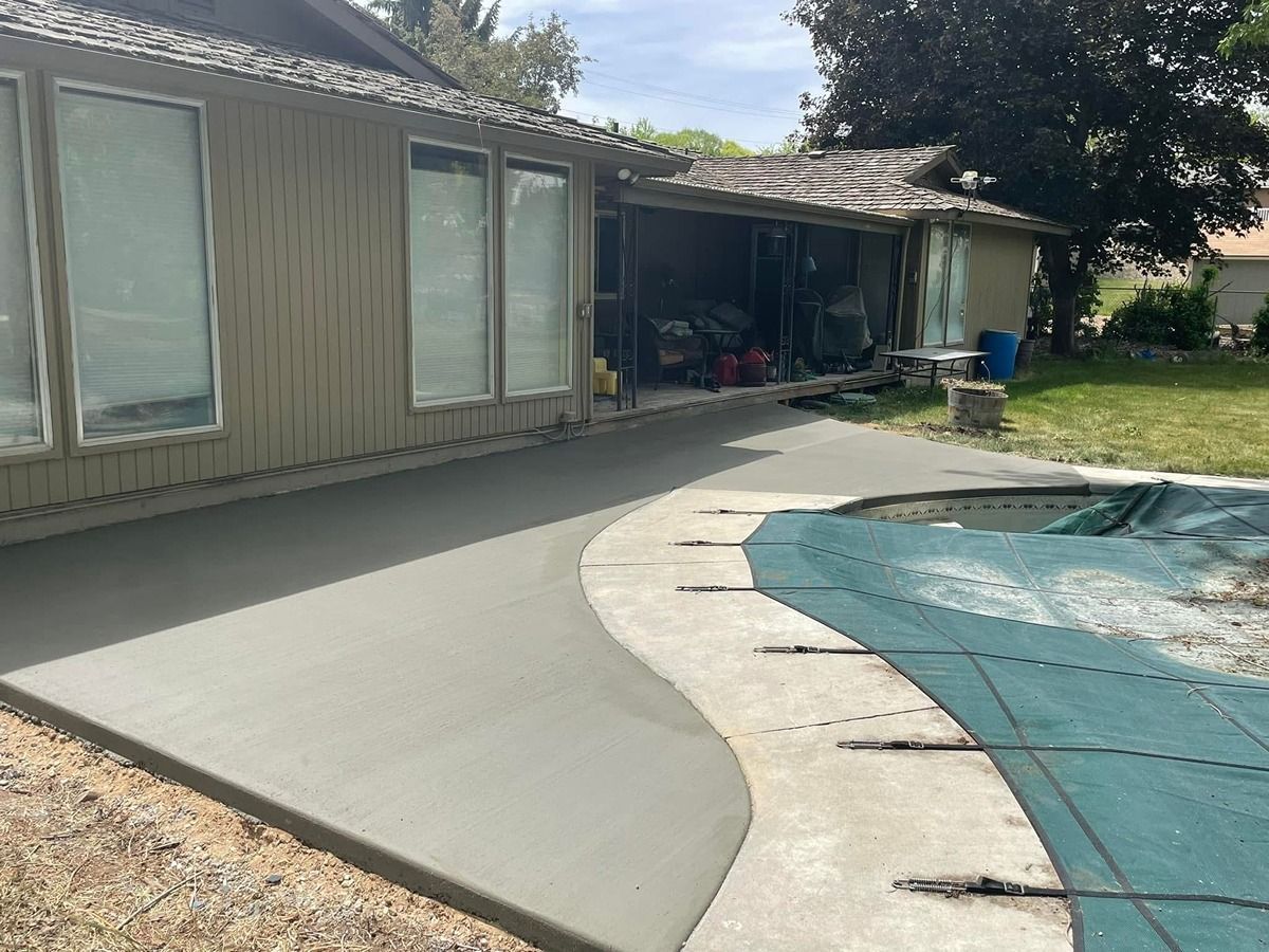 Backyard patio with fresh gray concrete curving around a covered pool.