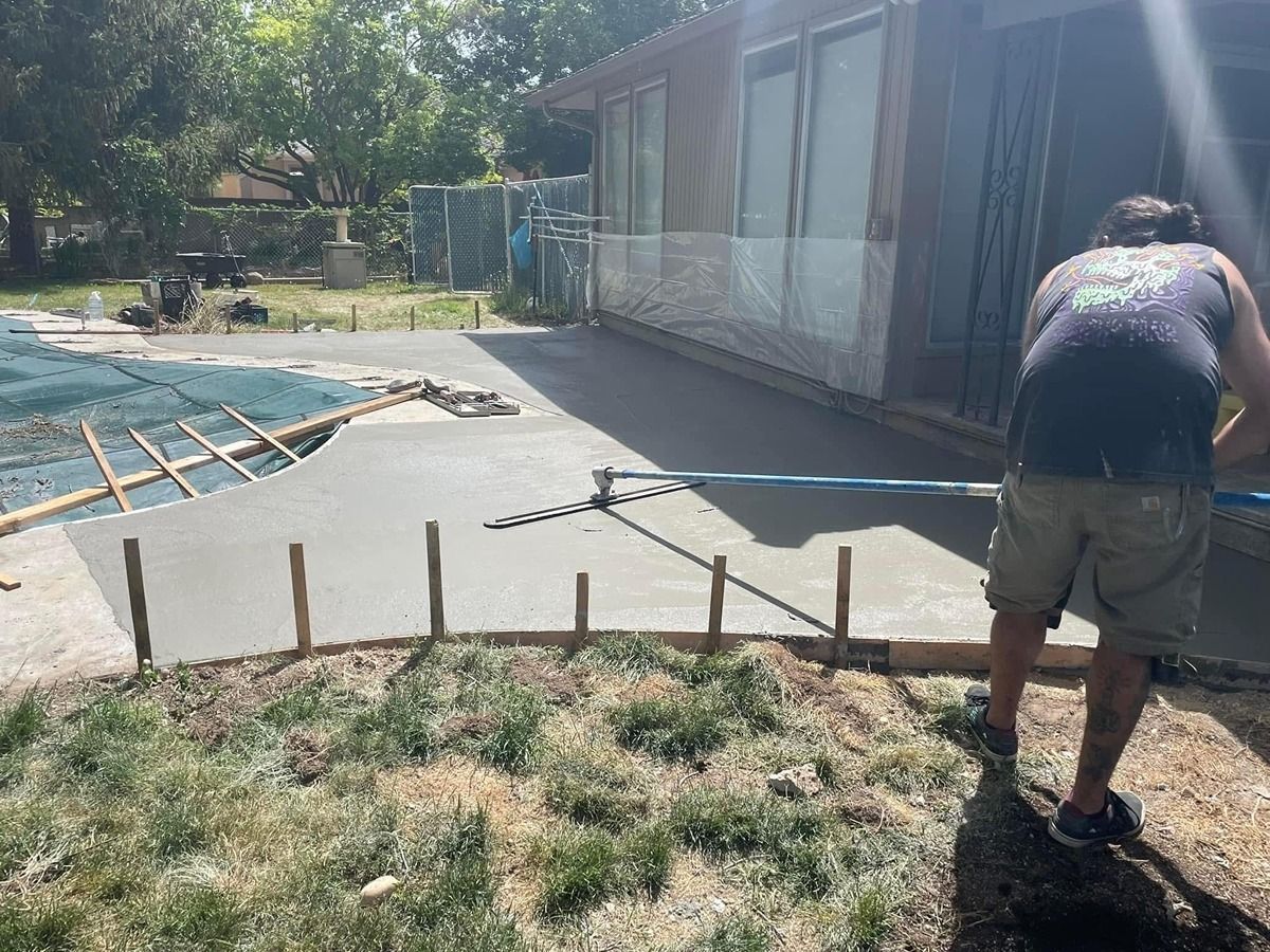 Backyard pool with a fresh concrete walkway being edged by stakes beside a person working.