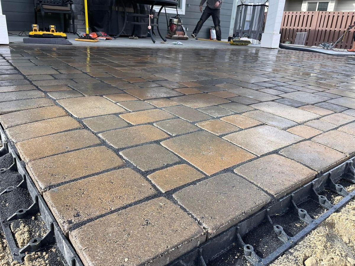 Wet brick paver walkway under construction beside a building, with workers in the background