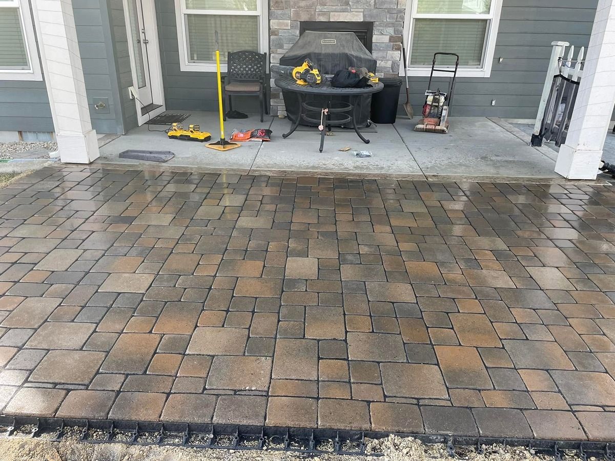 Patio with gray paver flooring, a black grill, and cleaning tools near the house entrance