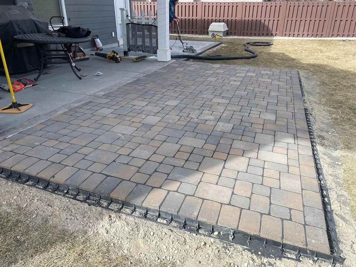 Paver patio beside a lawn, with a small covered grill area and fence in the background.