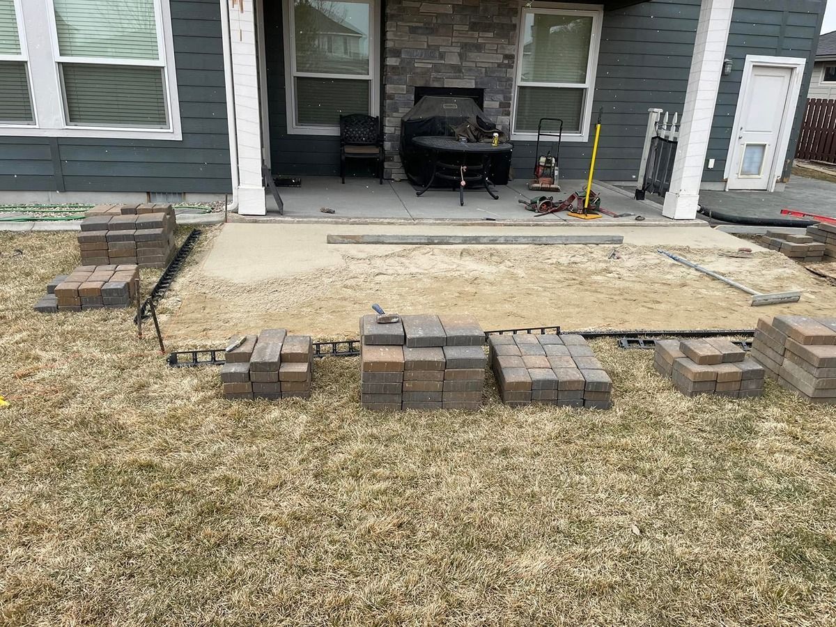Front porch with a newly outlined paver patio and stacked bricks in a yard