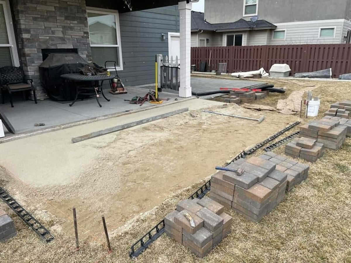 Backyard patio under construction with pavers, gravel, and a concrete slab beside a house