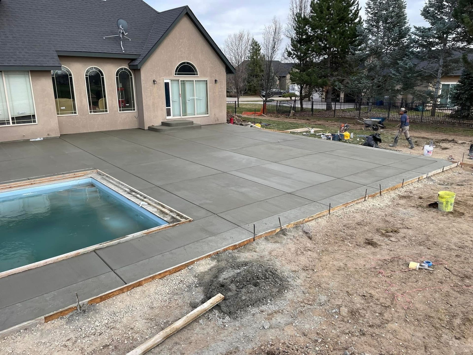 Backyard pool and patio beside a house, with a gravel yard and trees in the background