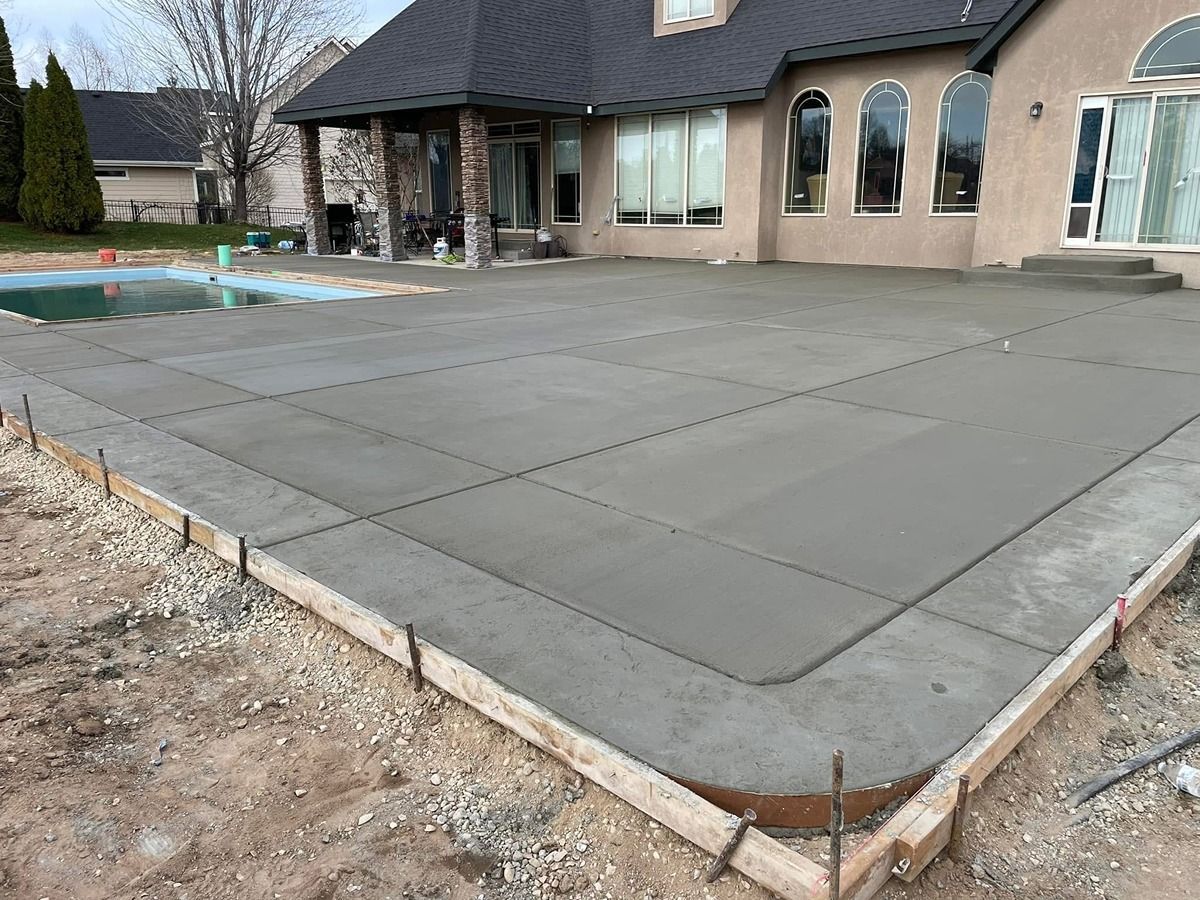 Freshly poured concrete patio in front of a house under construction, with forms and unfinished yard.