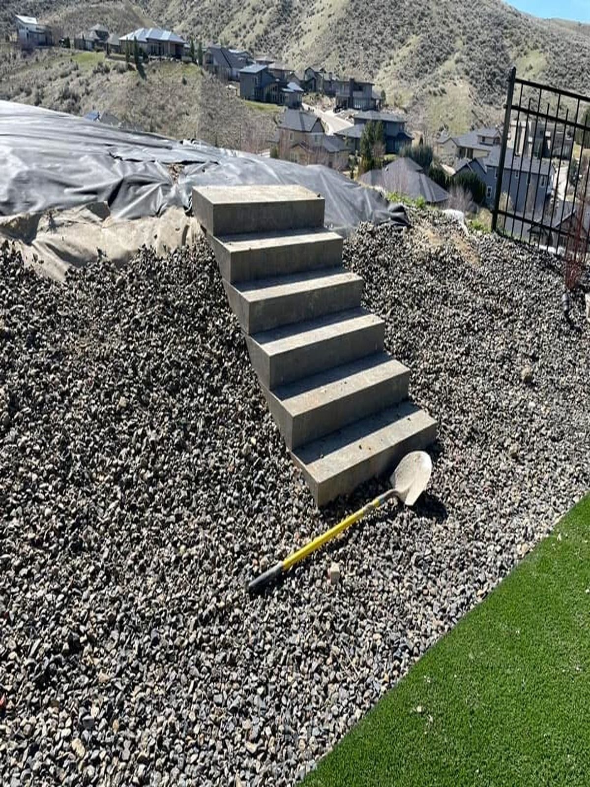 Small outdoor staircase in a gravel hillside garden beside a black fence and green lawn.