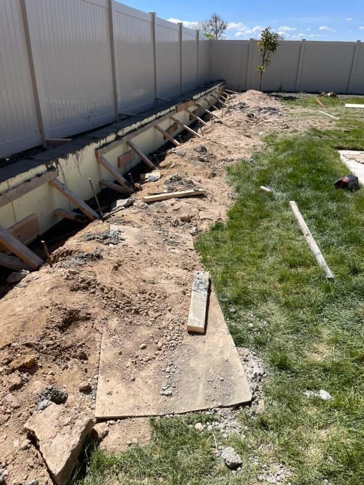 Backyard trench along a white fence with exposed soil and scattered construction boards