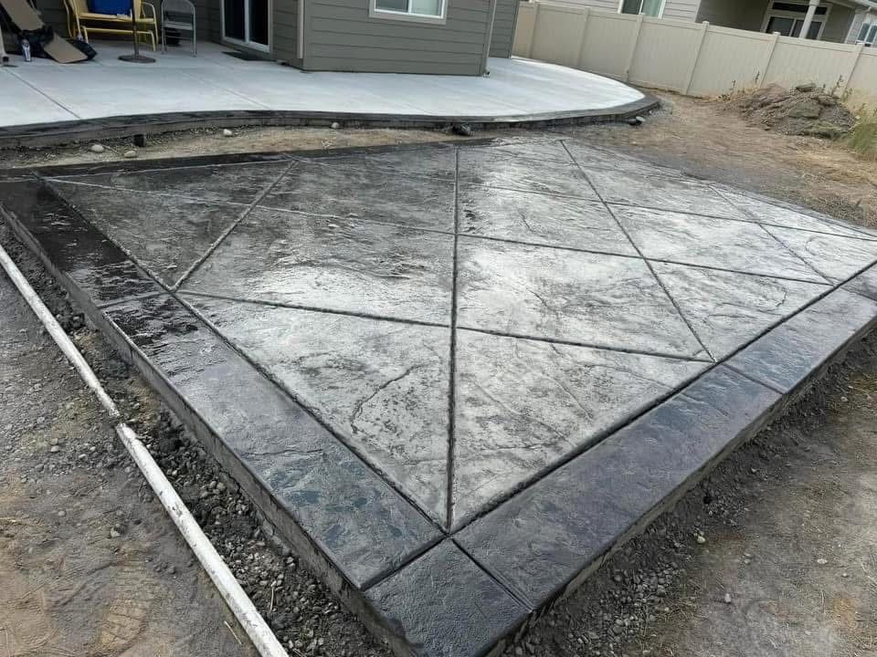 Stamped concrete patio under construction beside a house, with wet gray panels and dark border trim.