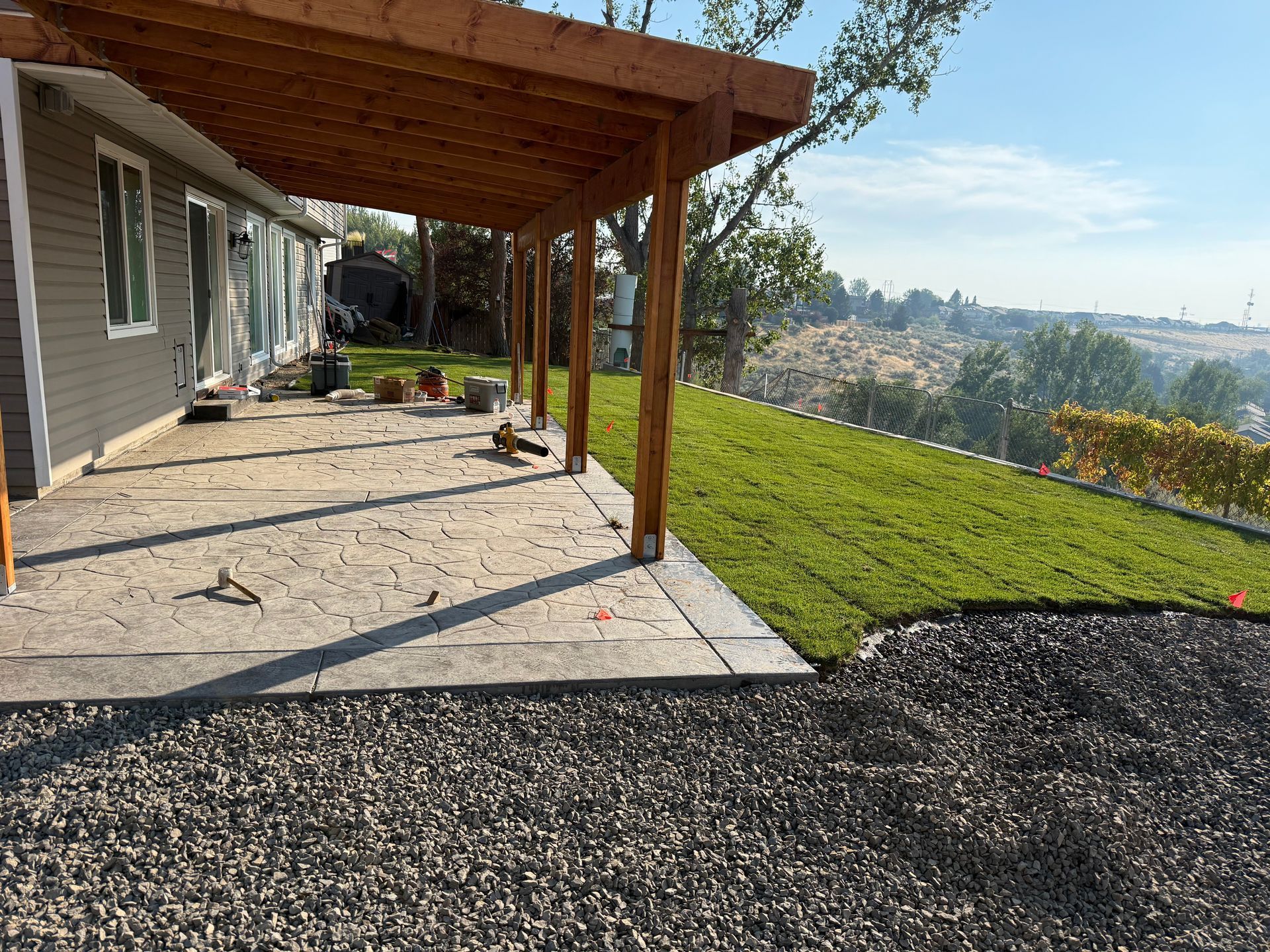 Patio beside a house with a wooden pergola, concrete slab, green lawn, and hillside view
