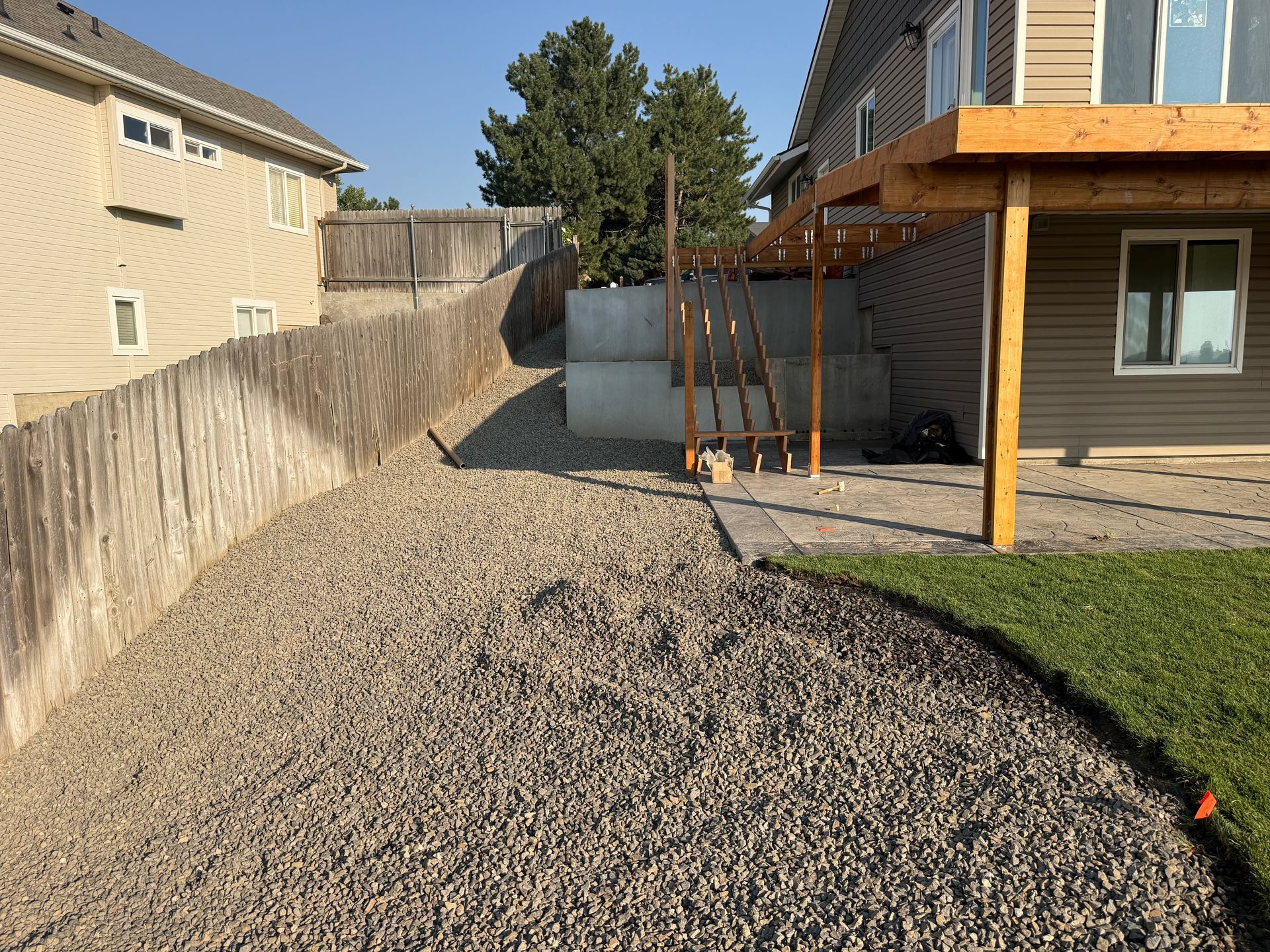 Backyard with gravel path, wooden fence, two houses, and a covered patio beside a patch of grass