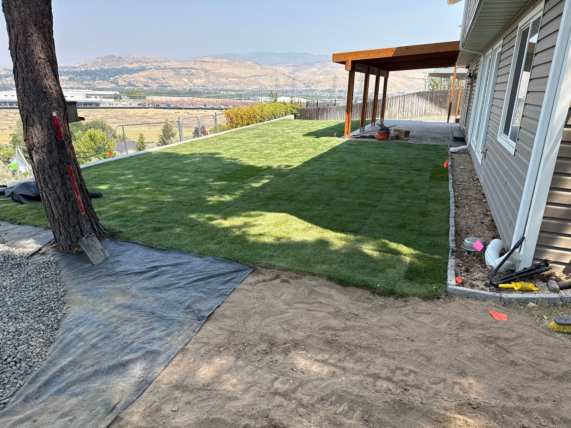 Backyard with green lawn, patio, hillside view, and gray house wall under a covered deck