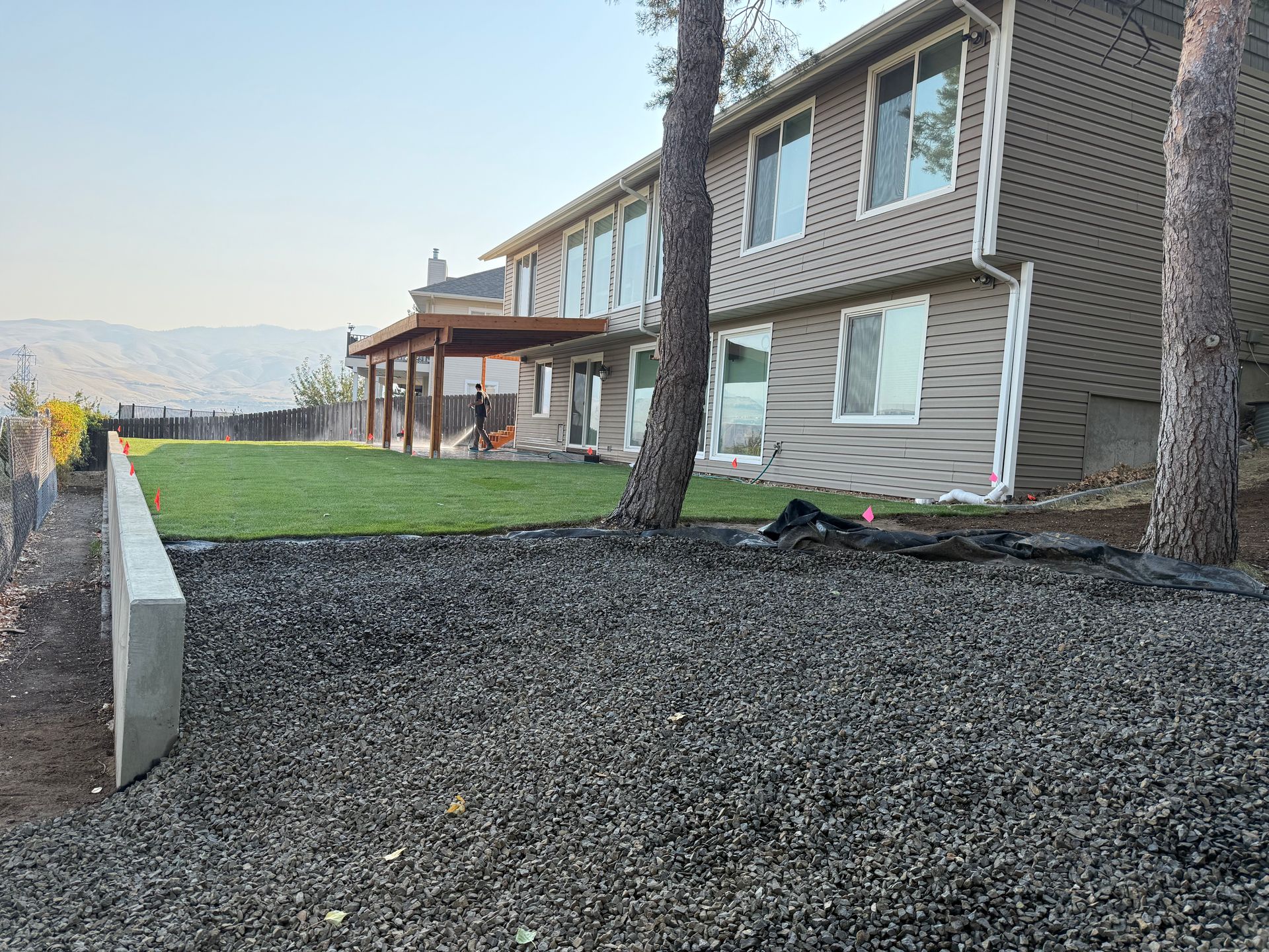 Apartment building with stone siding, gravel yard, grass lawn, and tall trees at sunset