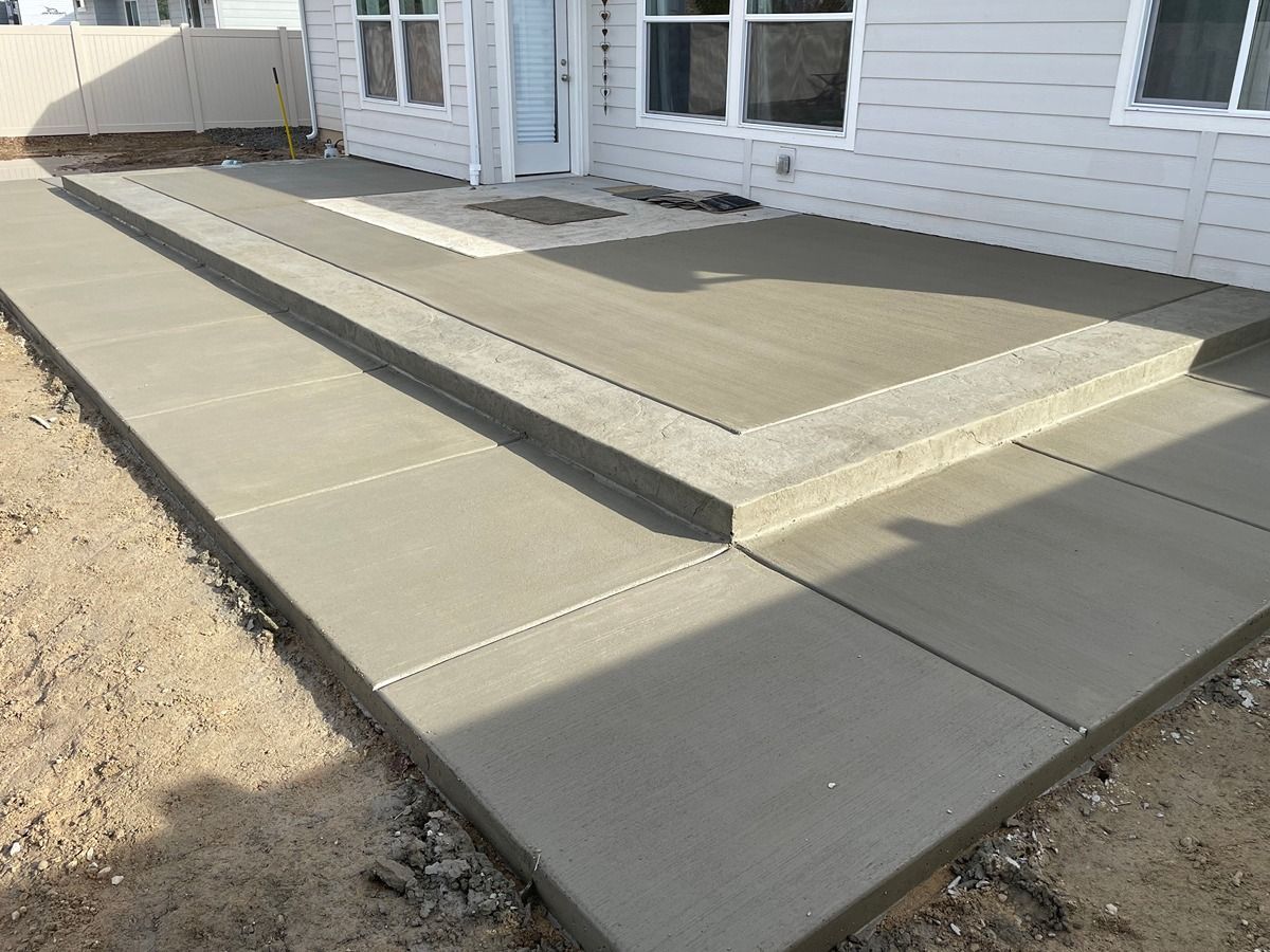 Concrete backyard patio and raised ramp leading to a white house with sliding glass doors.