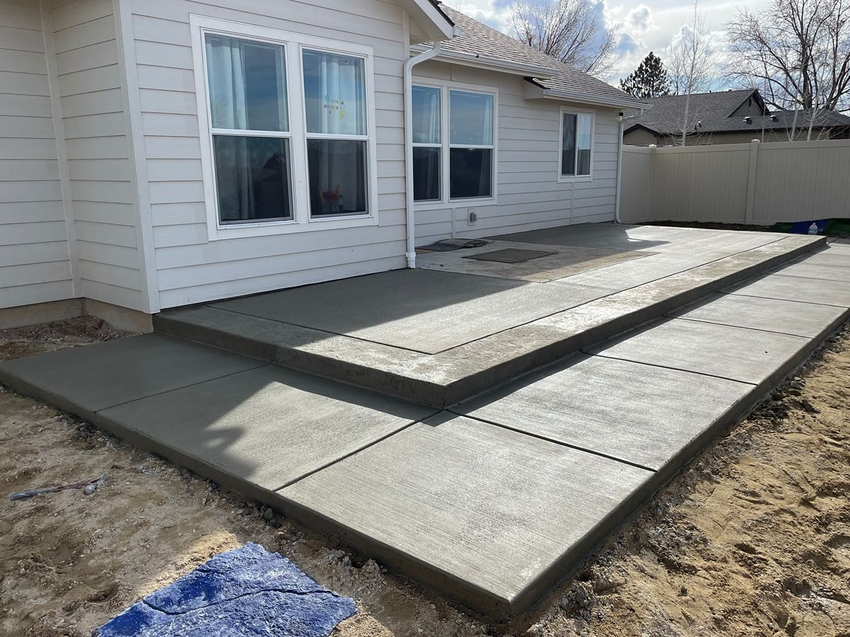 Concrete patio and ramp alongside a house exterior, with a fenced yard in the background.